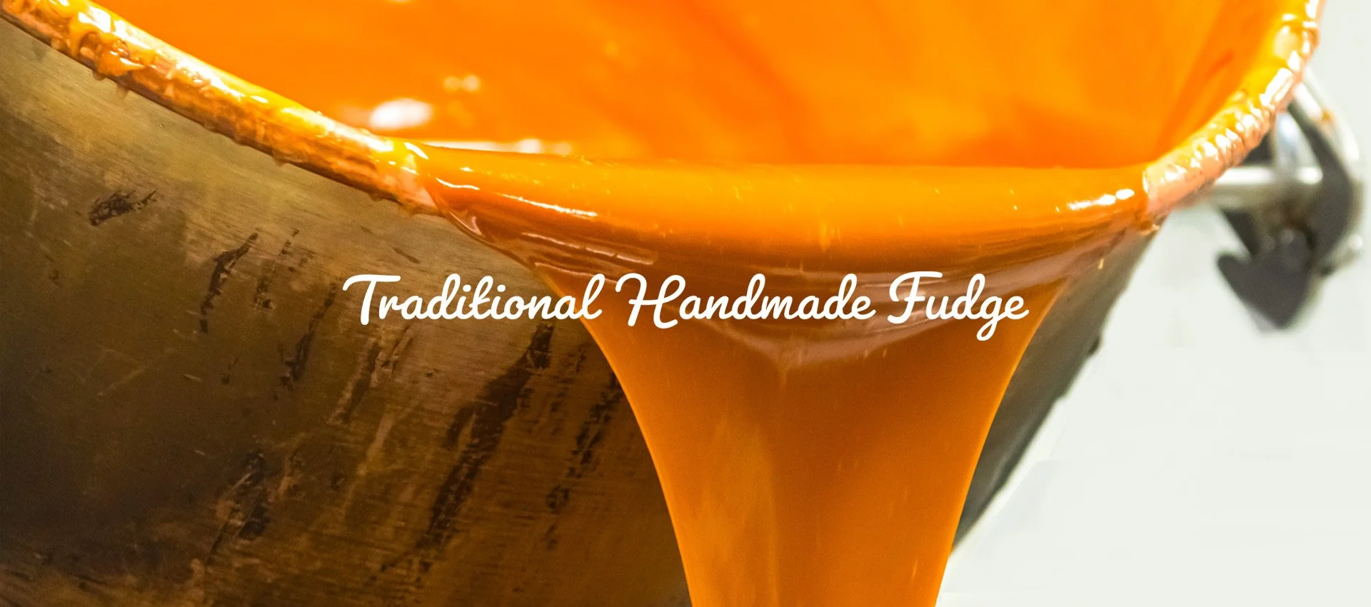 Close-up of traditional handmade fudge being poured from a copper pot, with the words 'Traditional Handmade Fudge' overlaid.