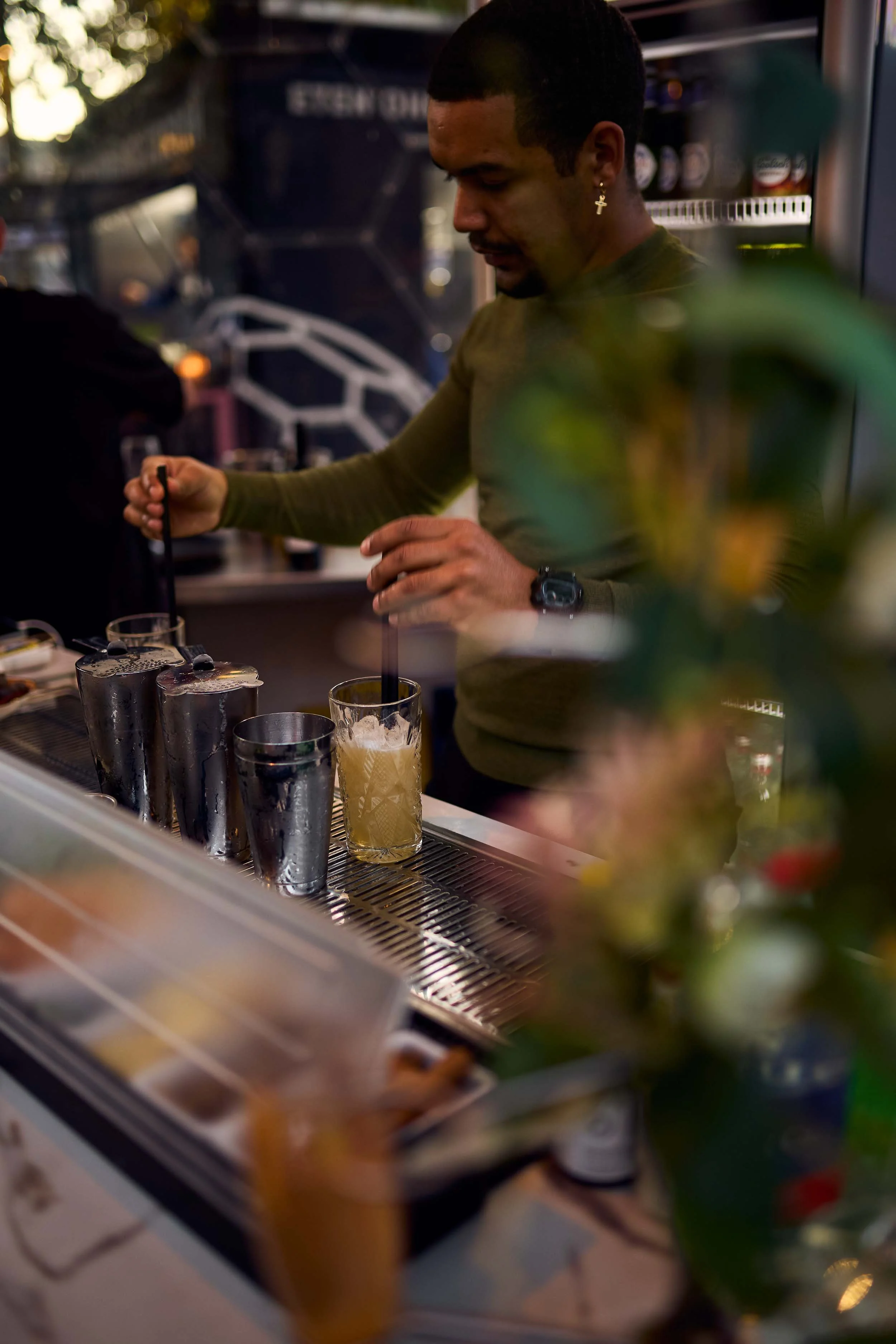 Barman maakt cocktails in een bar met een drankje en verschillende tools op de toonbank, terwijl er decoraties en glazen op de achtergrond te zien zijn.