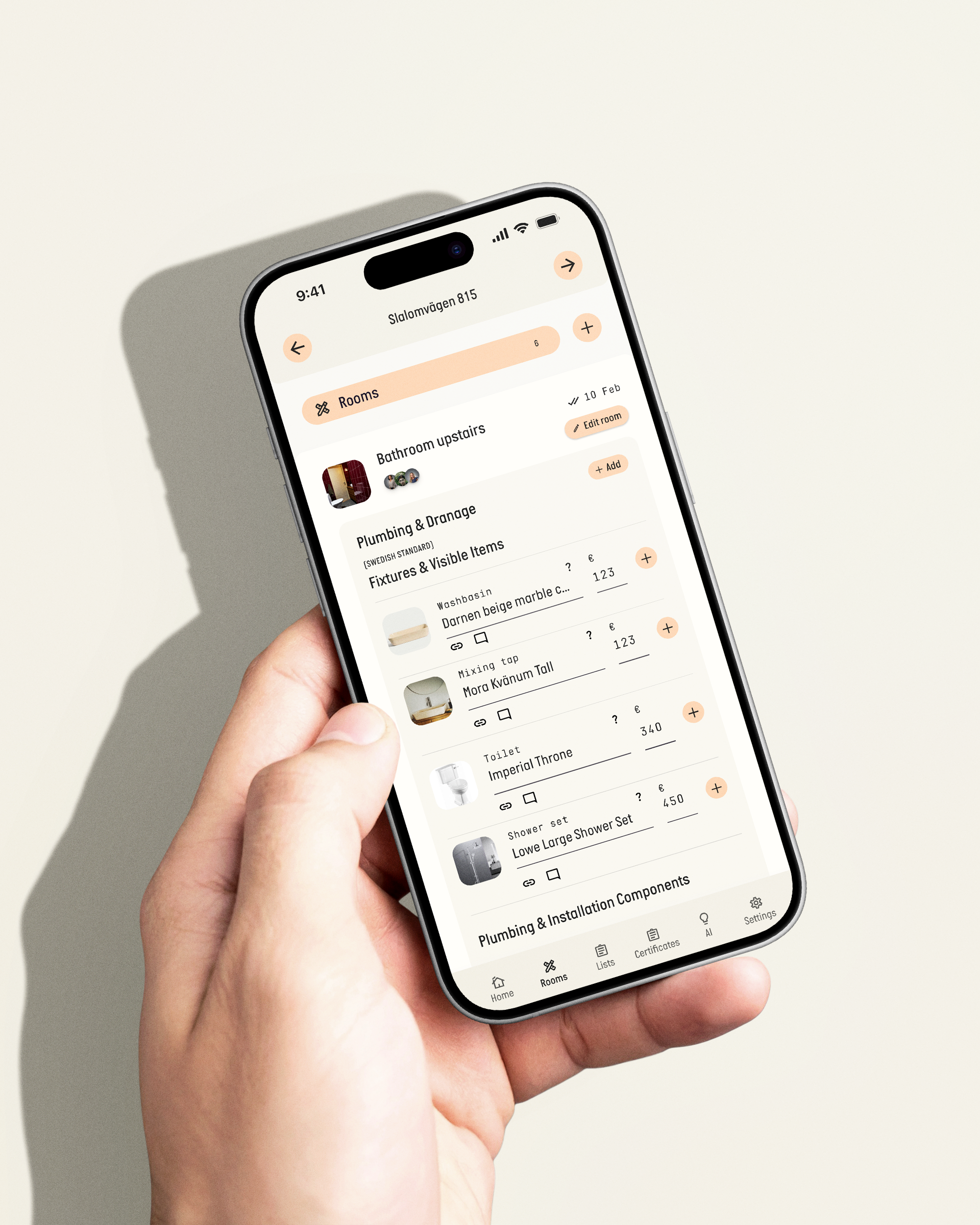 En hand håller en smartphone som visar en applikation för rums- och inventariehantering, med olika rum och objekt listade.