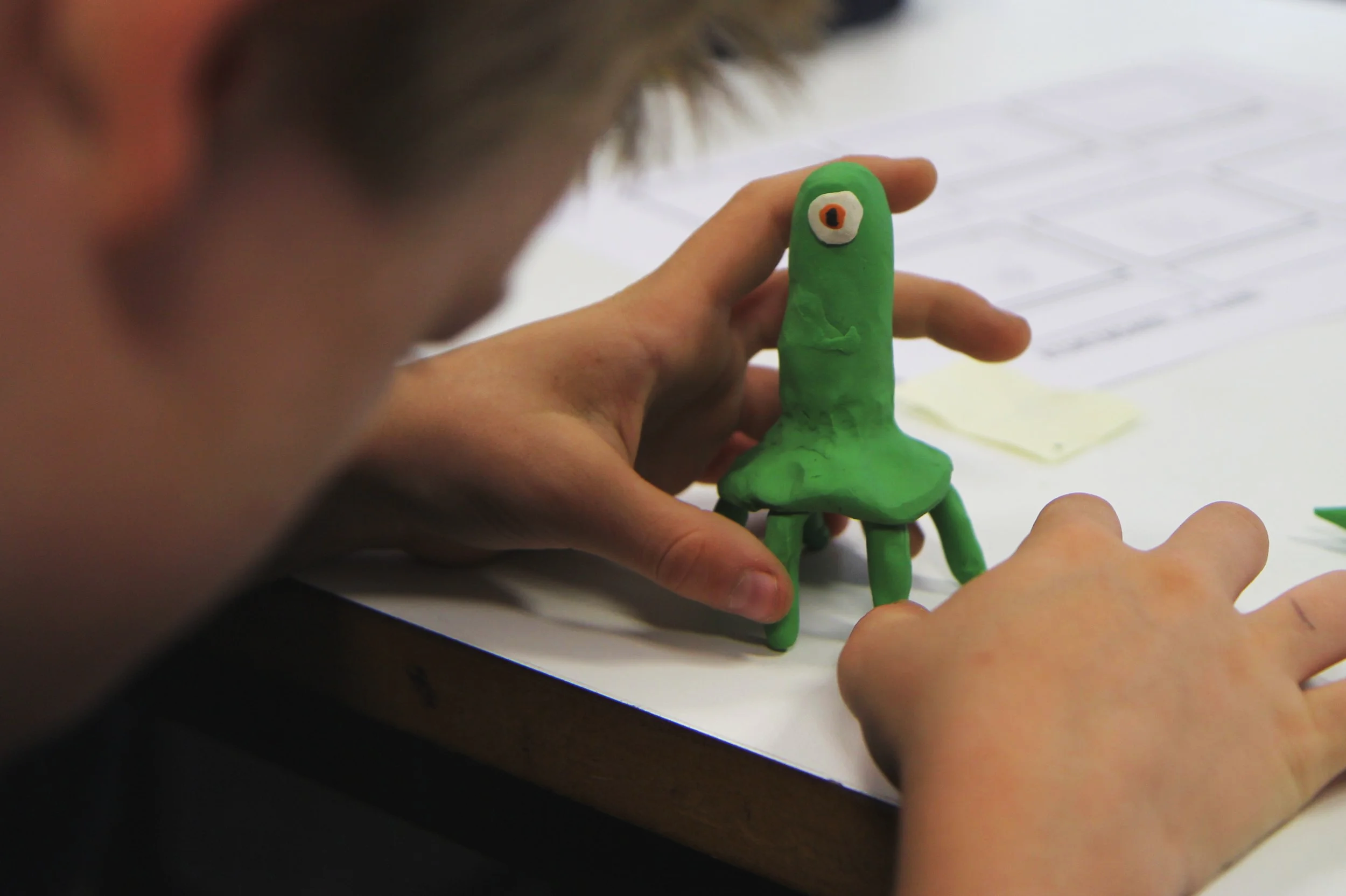 Child making a green clay creature with one eye at a table.