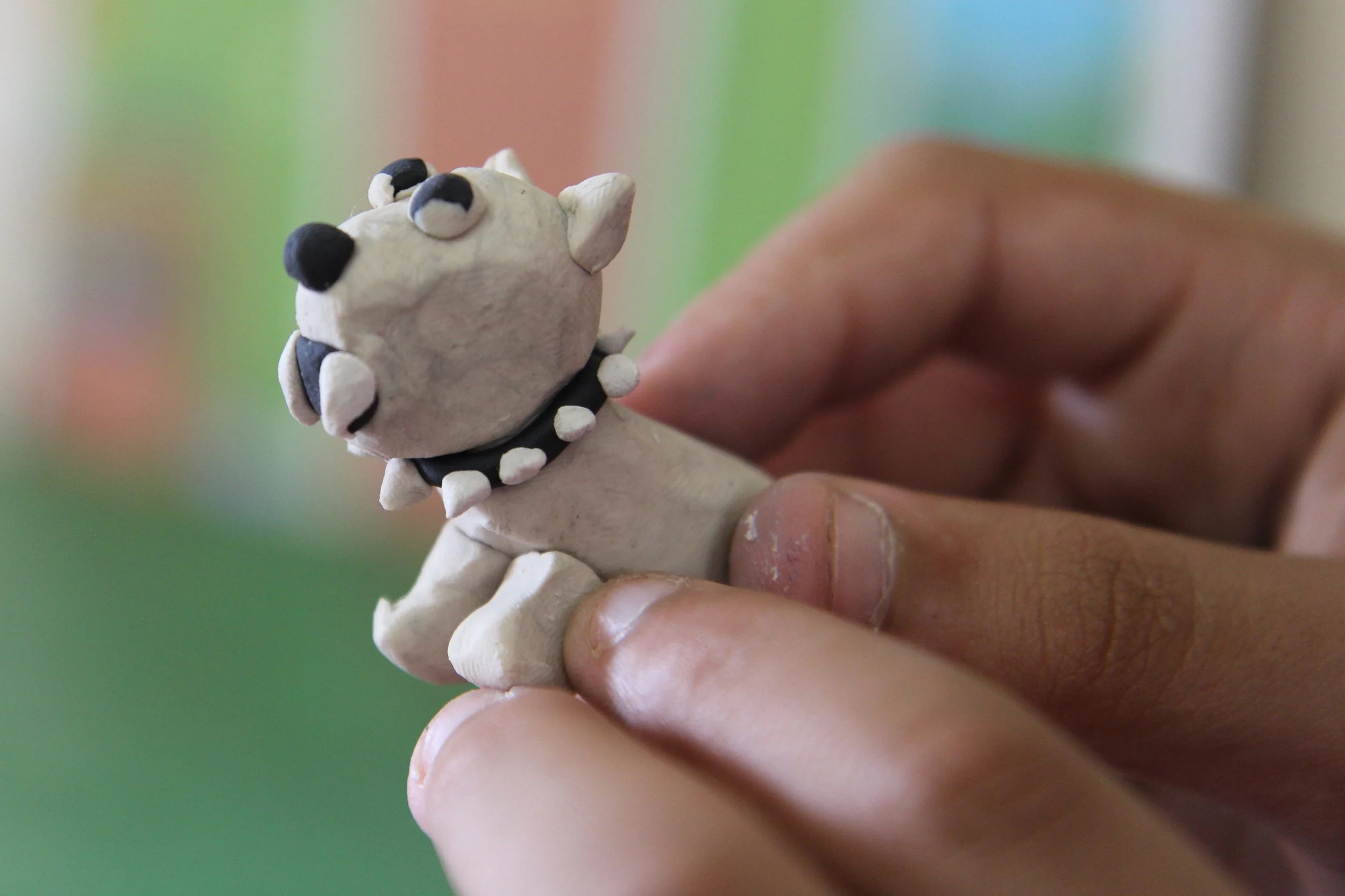 Hand holding a small, nose, eyes, and mouth decorated miniature model of Bowser from Super Mario, with a spiked collar on a colorful blurred background.
