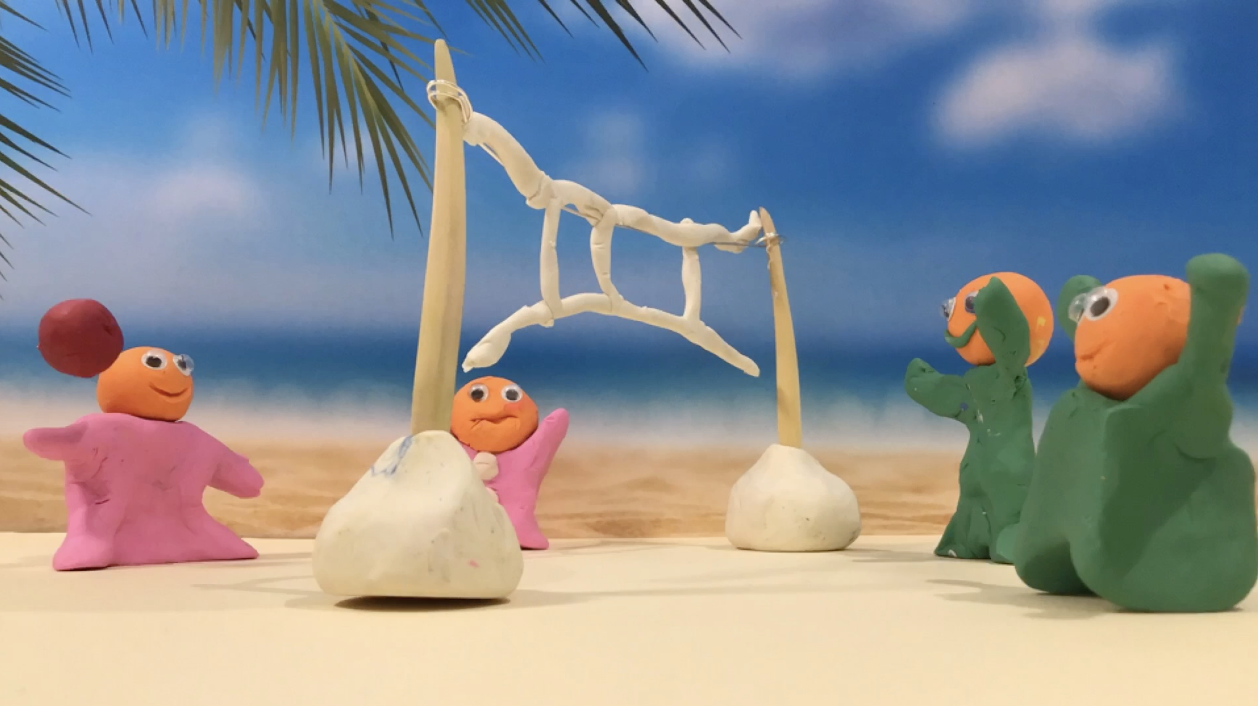 Colorful clay figures resembling characters on a beach with a blue sky and ocean in the background. One figure with an orange head and pink body swings on a wooden and fabric swing, while three other figures with orange heads and green or pink bodies