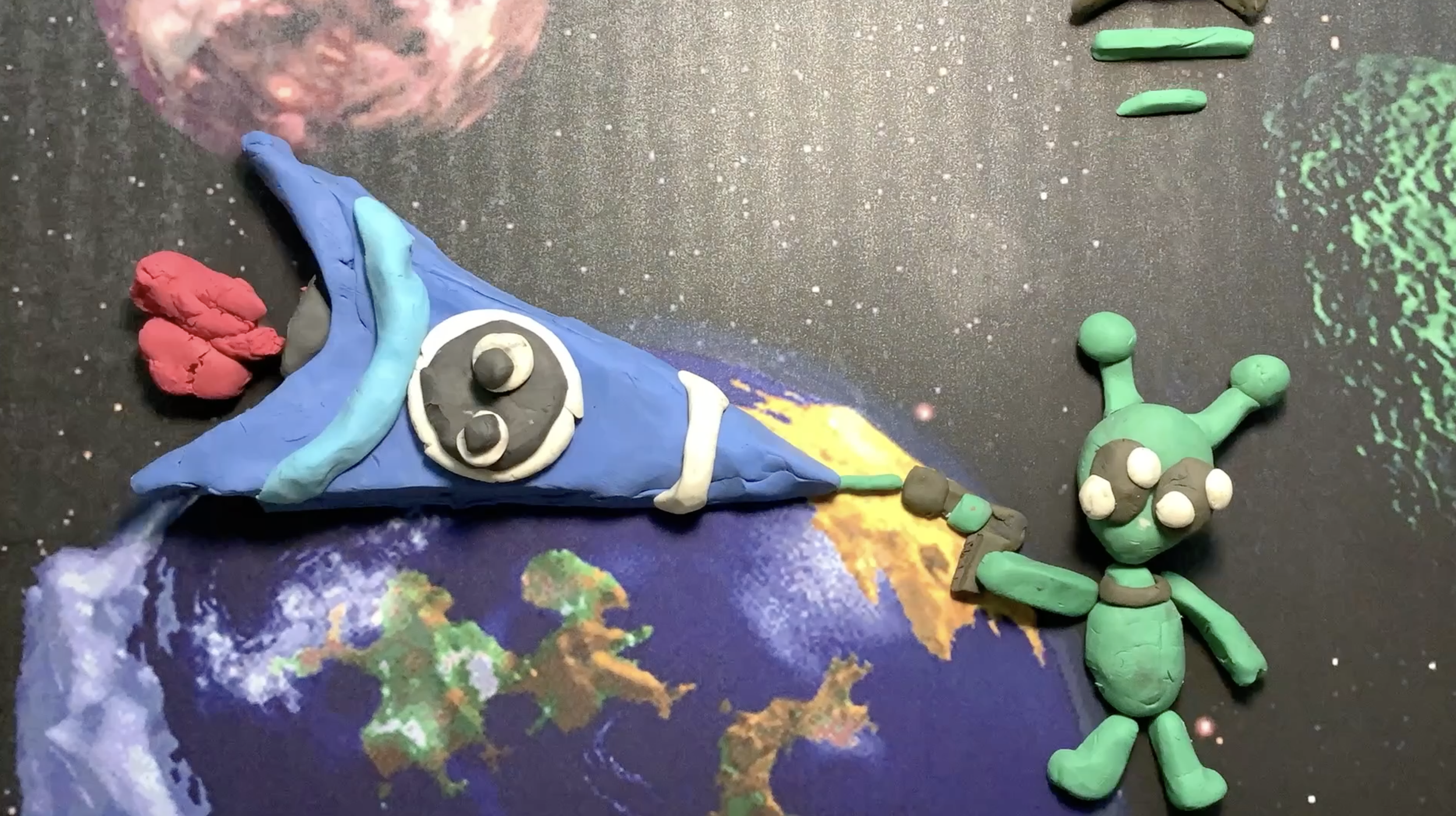 Clay models of a wizard with a blue hat and robe, a gray face with large eyes, and a green alien with three eyes and antennae, set against a space-themed background.