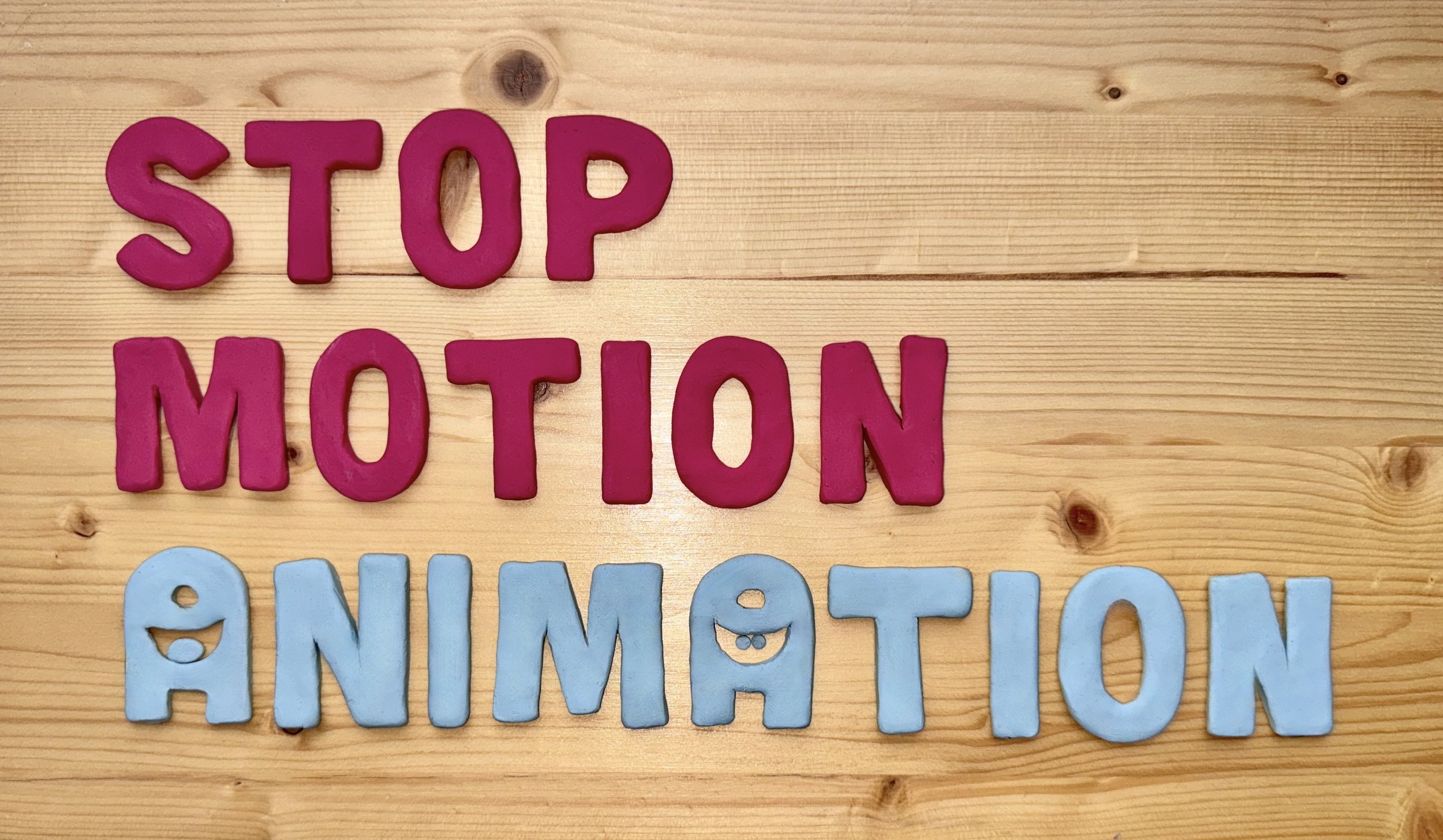 Colorful foam letters on wood spell out "STOP MOTION ANIMATION" with a smiley face inside the 'O' of "ANIMATION".
