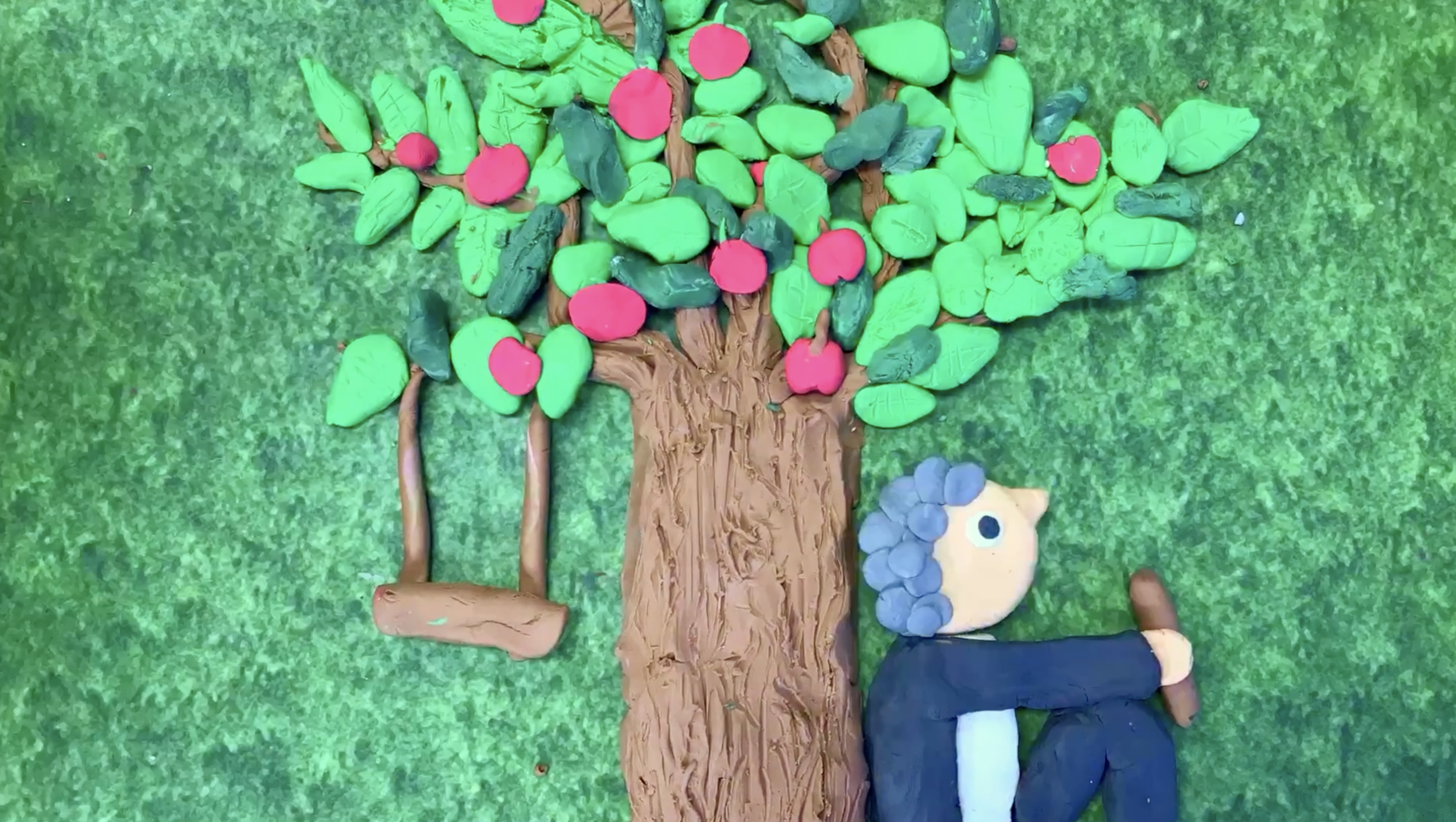 A colorful clay art depiction of a person with blue hair, sitting under a large tree with green leaves and pink and red fruits, on a green background.