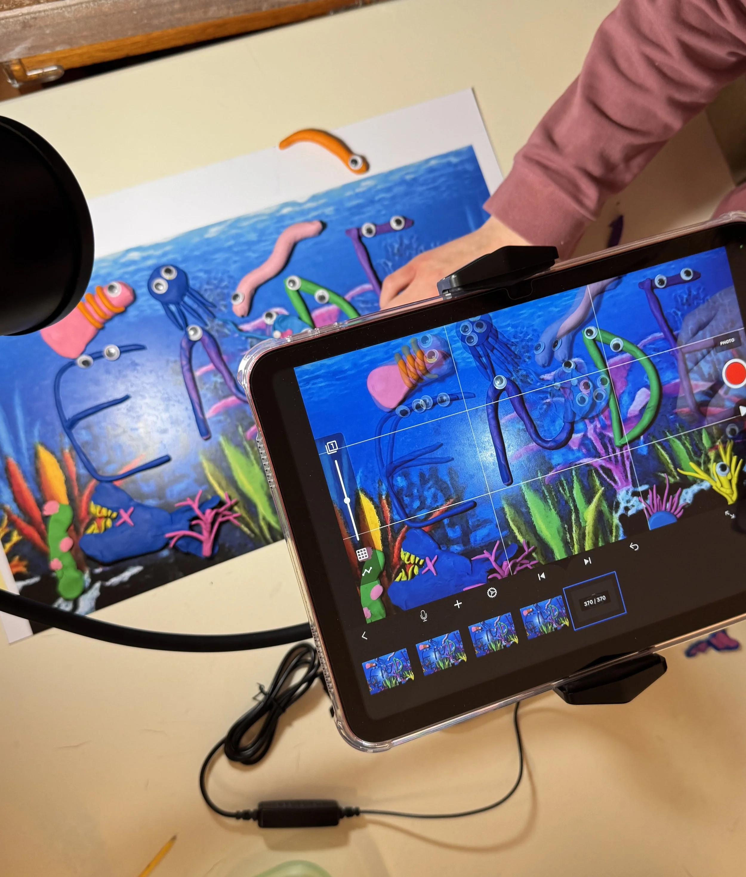 A video recording of an underwater-themed artwork, featuring colorful sea creatures such as octopuses, worms, and coral, with a person filming it with a smartphone.