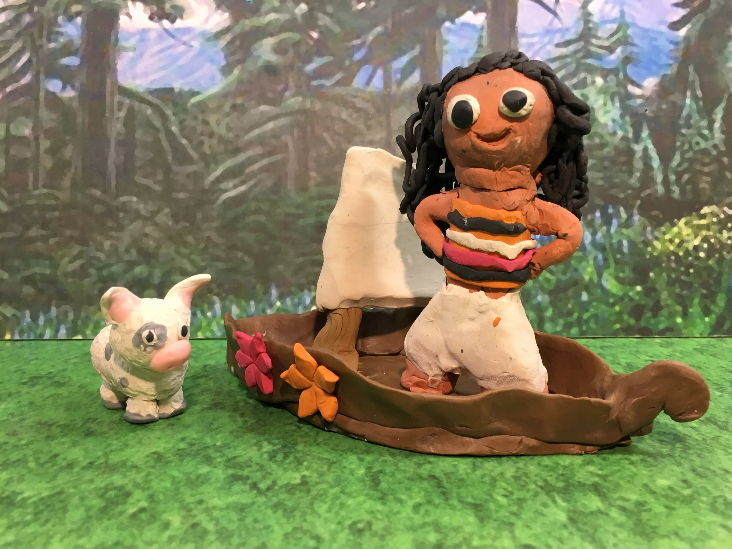Clay sculpture of a woman stands in a small boat with flowers, alongside a pig sculpture, set against a painted forest background.