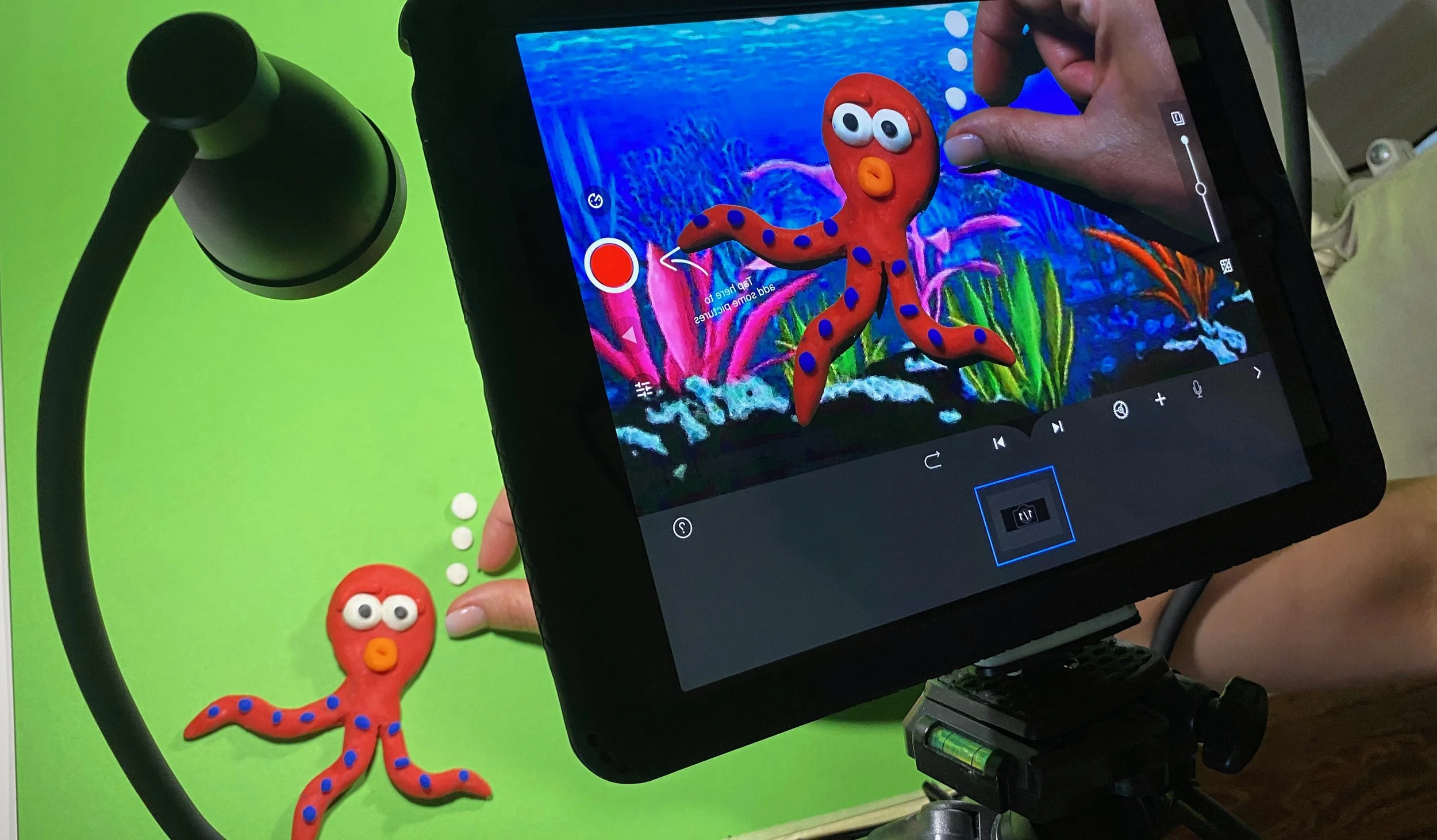 A tablet being used to record a stop-motion animation of a red clay octopus with purple spots and big eyes, set against a colorful underwater background.