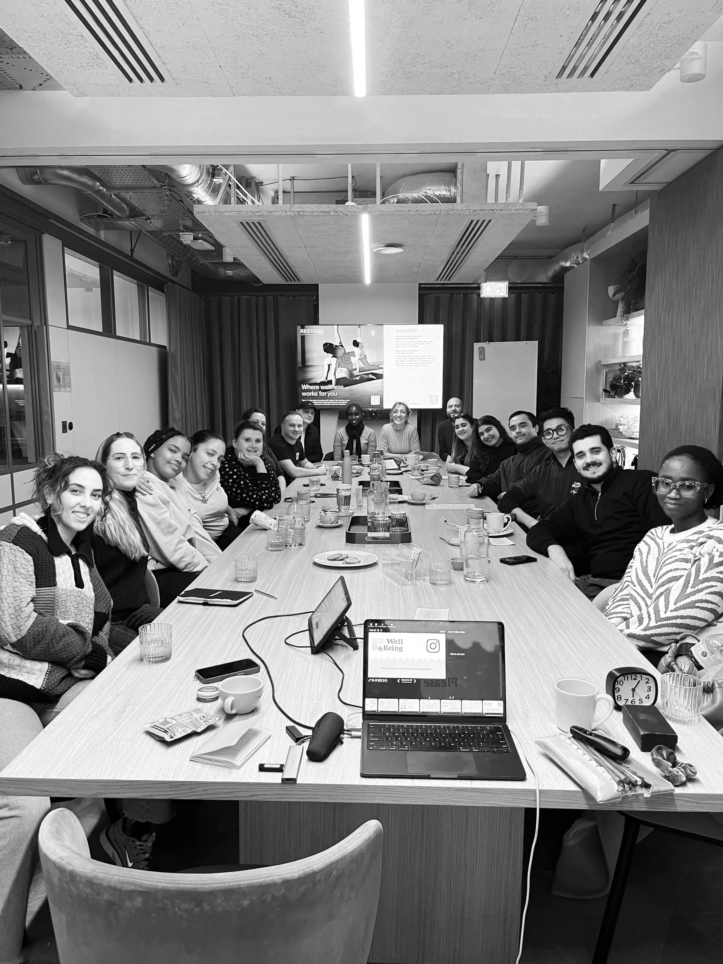 Group of diverse people sitting around a conference table in a modern office meeting room, smiling and looking at the camera.