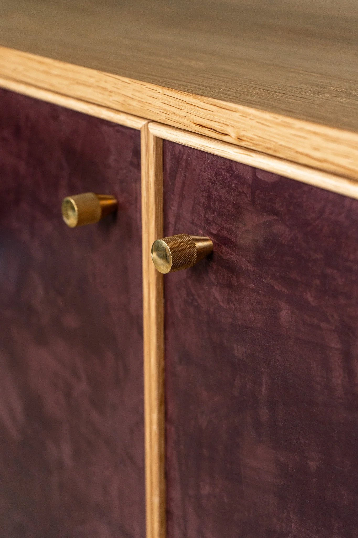 Close-up of a solid handmade white oak cabinet with a hand-troweled deep burgundy plaster finish with visible texture and two brass knobs.