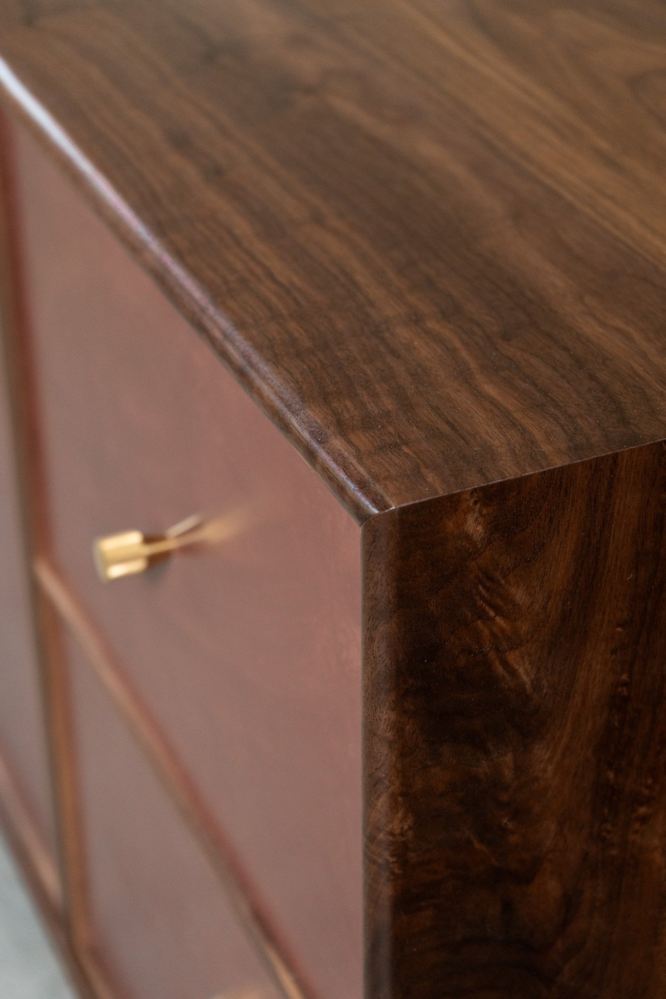 Close-up of a solid walnut sideboard cabinet with a burgundy hand-troweled plaster front, solid unlacquered brass knobs, and rounded edges.