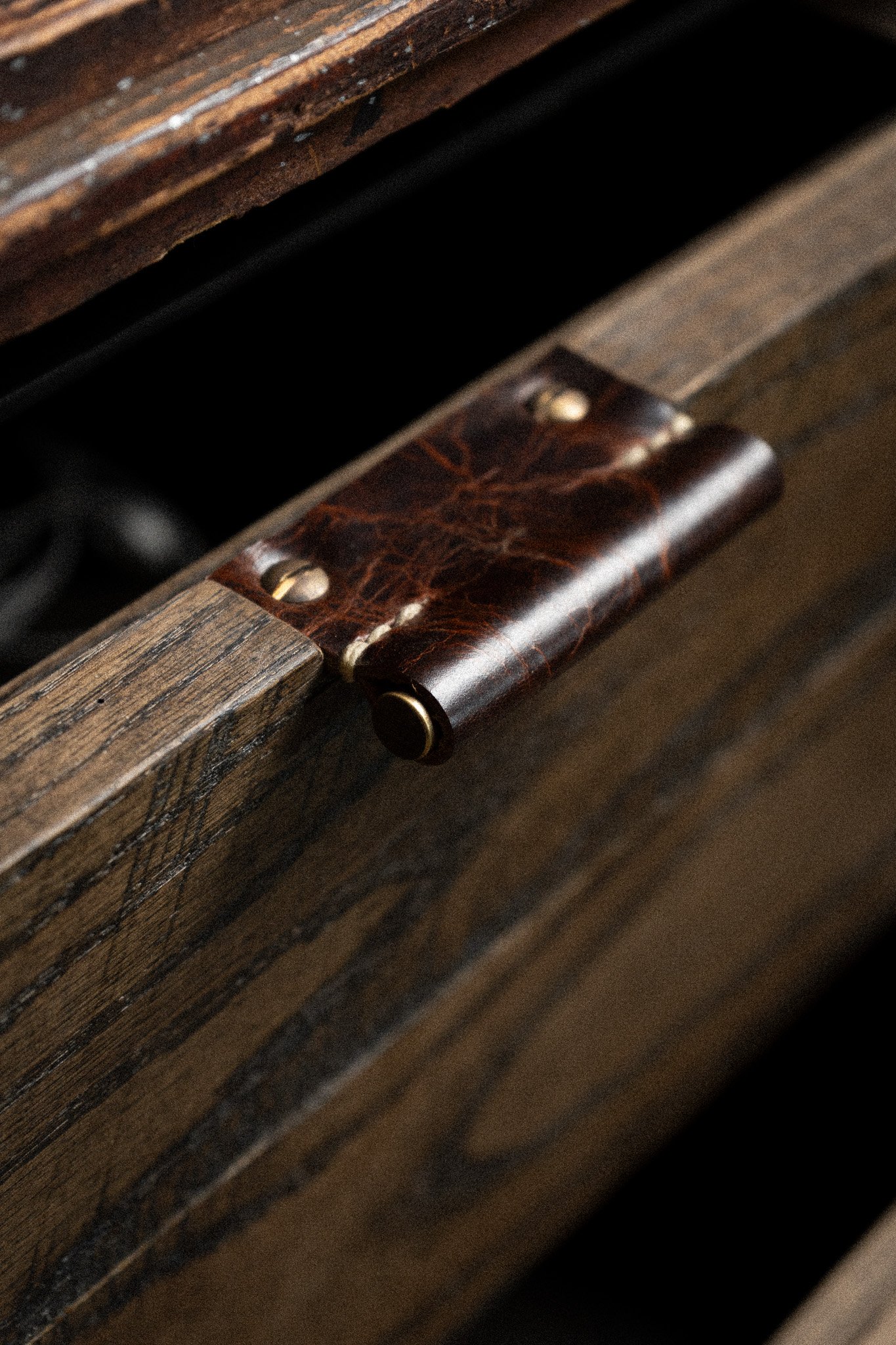 Close-up shot of a wooden drawer with a handmade, hand stitched leather pull with solid brass inlay and brass screws.