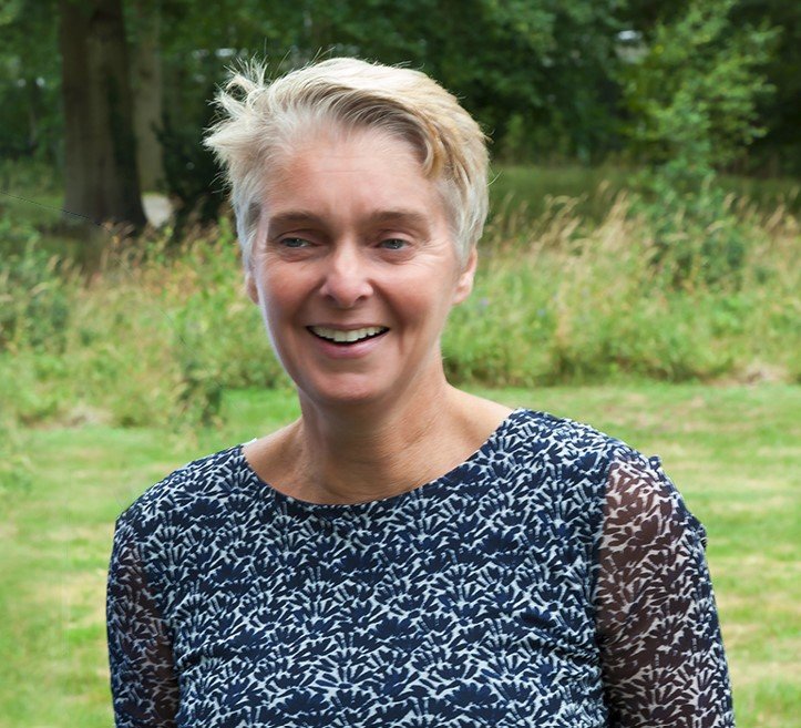 Vrouw met kort haar glimlacht naar de camera, tegen een witte achtergrond.