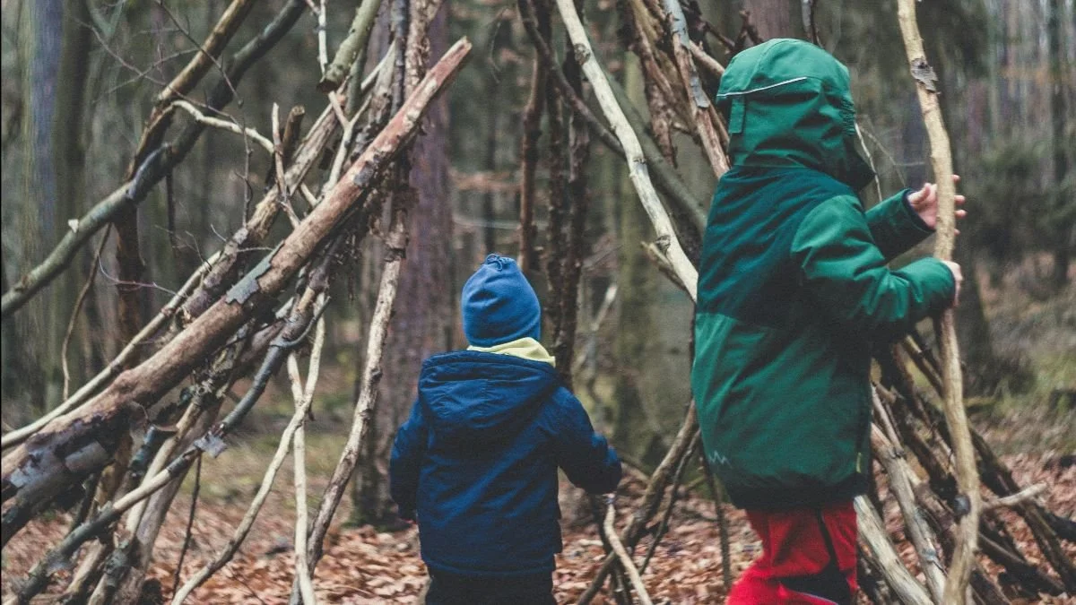 Twee kinderen bouwen een hut van takken in het bos.