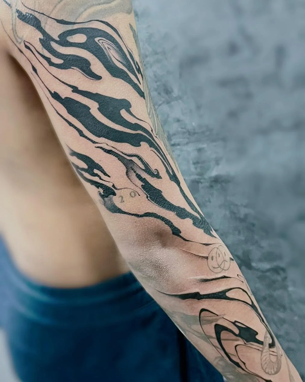 A person's arm with a tattoo of a tiger's head in black ink, along with a smaller face and other designs.