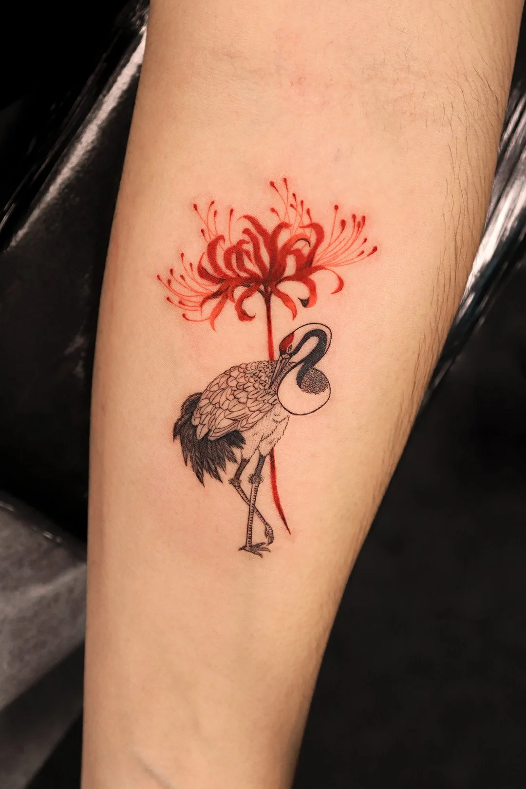 Tattoo of a flamingo with a red flower growing from its neck on a person's arm.