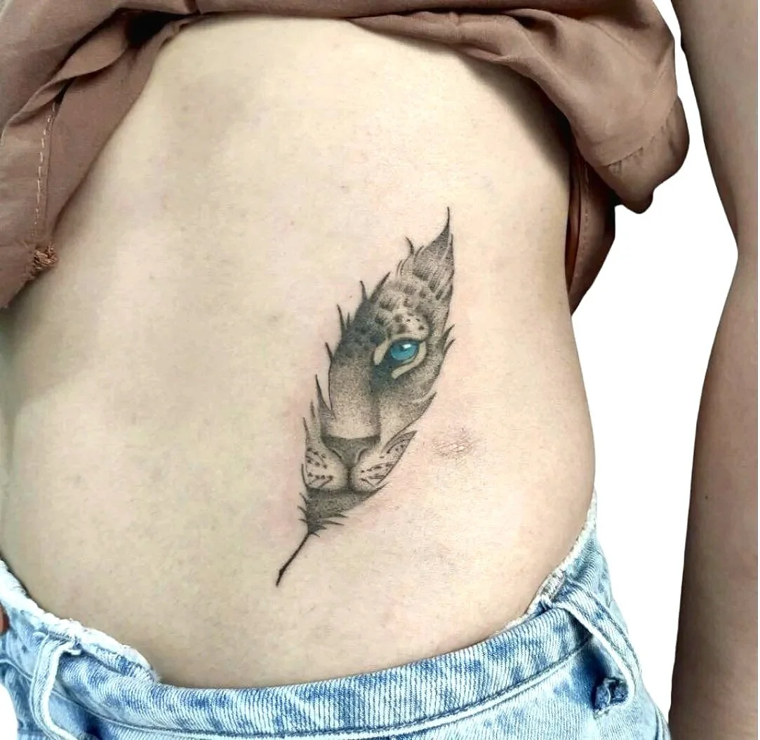 Tattoo of a tiger's face on a person's side, with the tiger's eye appearing blue, and the design resembling a feather.