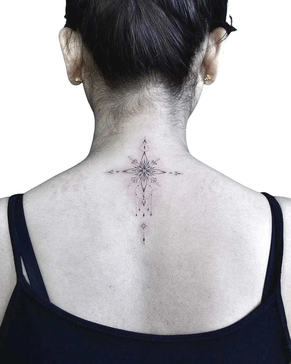 A woman with short dark hair, wearing a black spaghetti strap top and gold earrings, showing the back of her neck and upper back. She has a black ink tattoo of a floral mandala design on her neck.