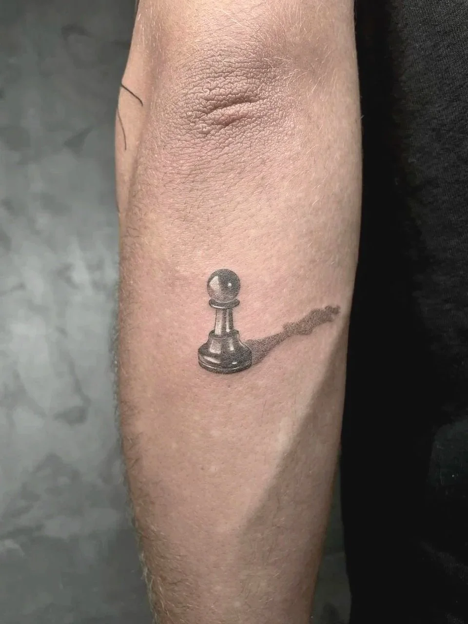 Tattoo of a chess pawn casting a shadow on a person's inner forearm.