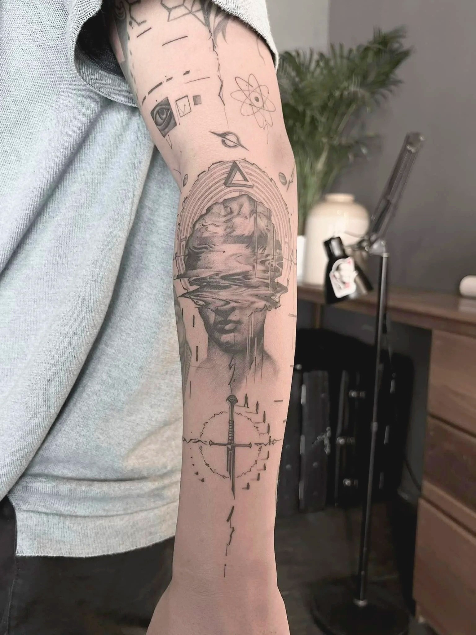 Tattoo sleeve featuring a distorted soldie's face with a landscape background, a sword, and various geometric and symbolic designs.