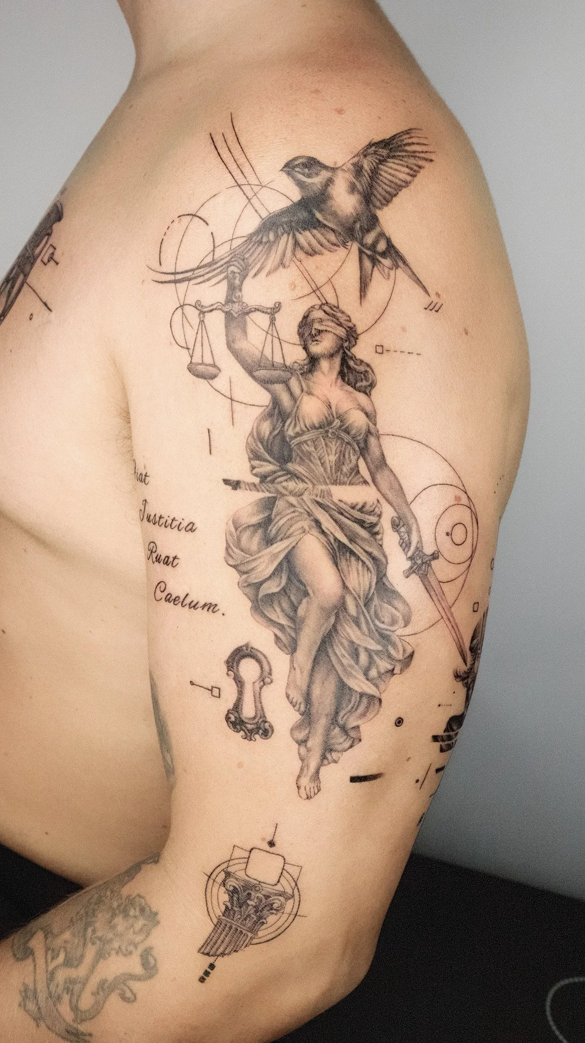Tattoo of a woman holding a sword, with a flying hummingbird above her, surrounded by geometric shapes and technical diagrams.