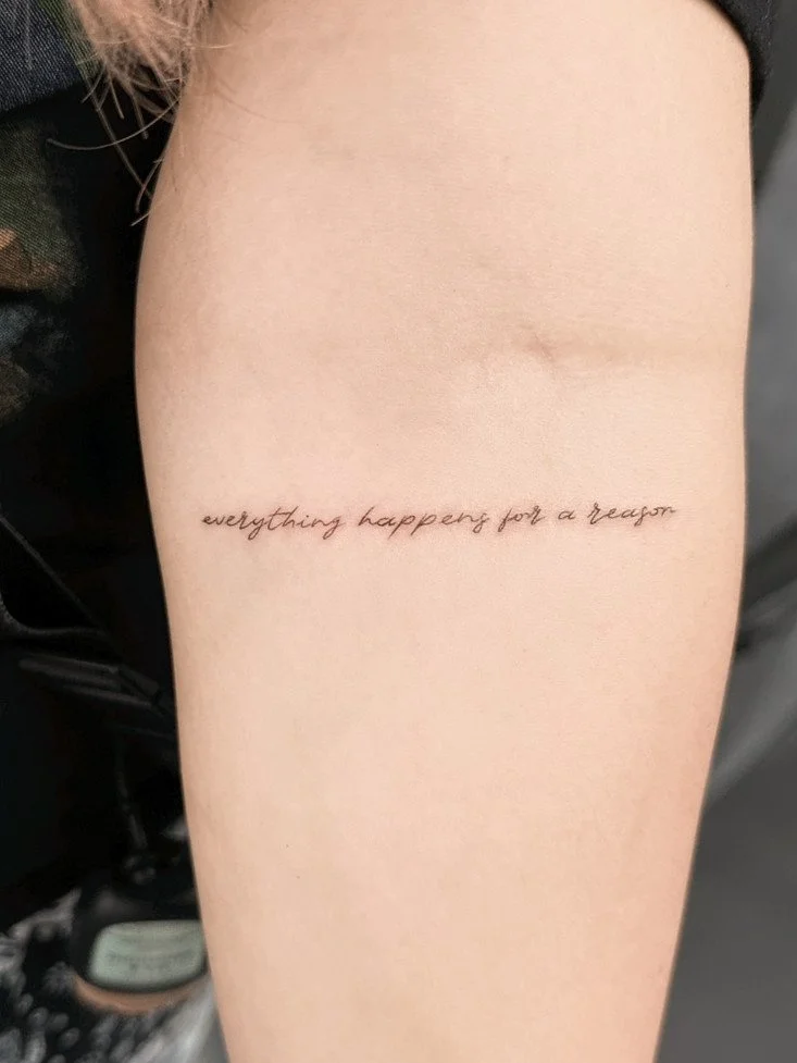 Tattoo on person's upper arm with the phrase 'everything happens for a reason' written in cursive.