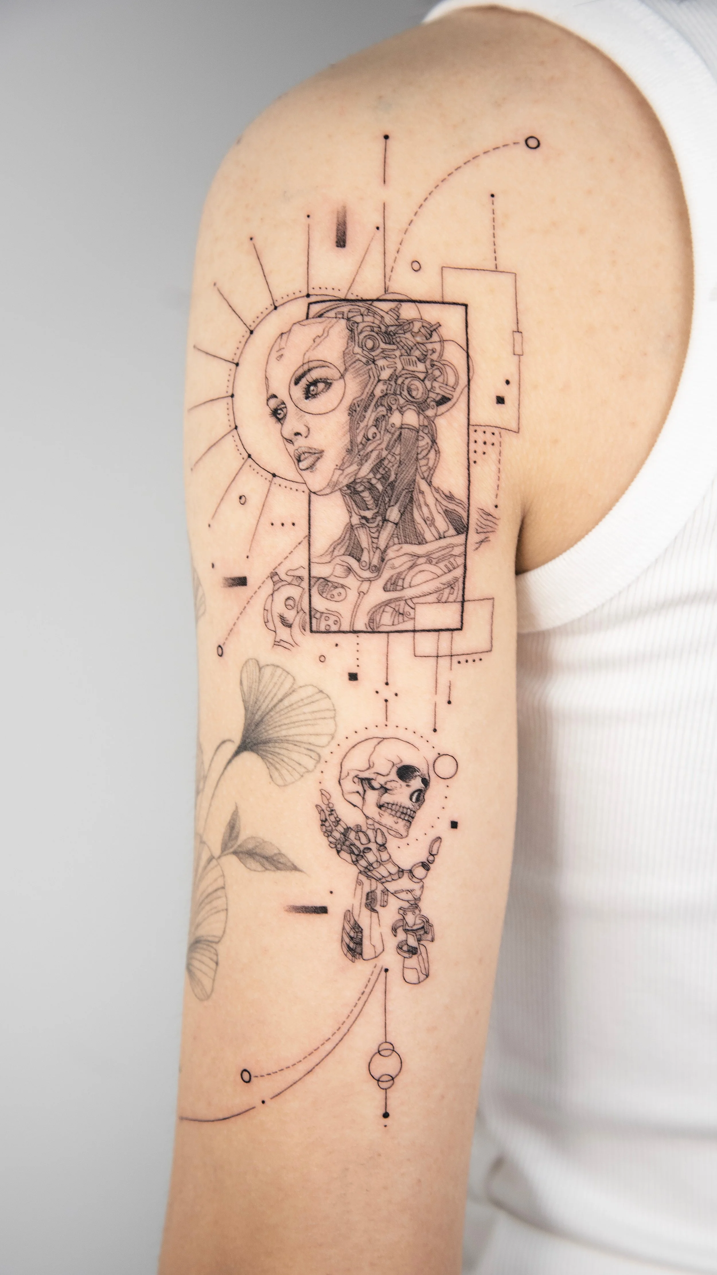 Tattoo of a futuristic woman with glasses, mechanical elements, and a robotic skull, with geometric and scientific-style accents, on the upper arm.