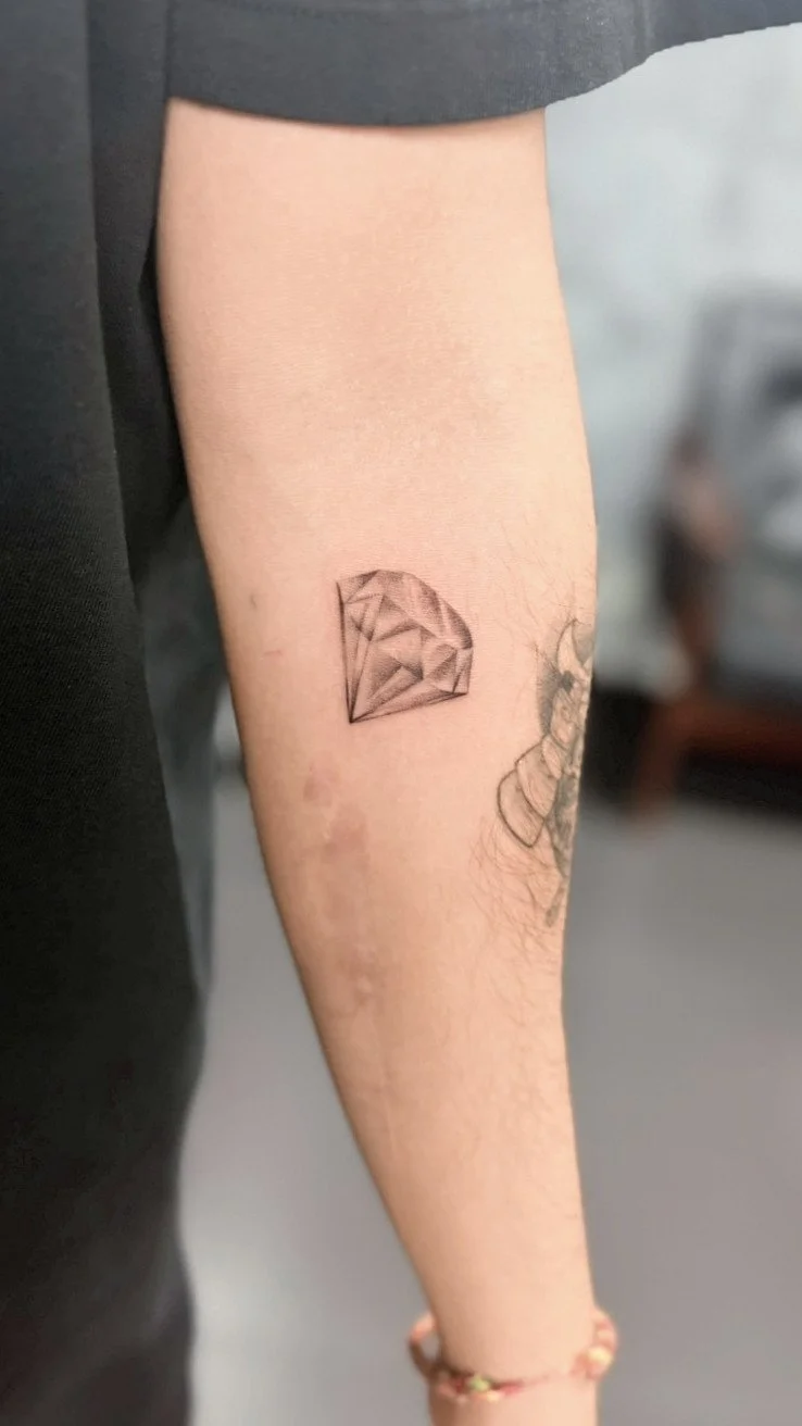 Tattoo of a detailed diamond on the inner forearm.