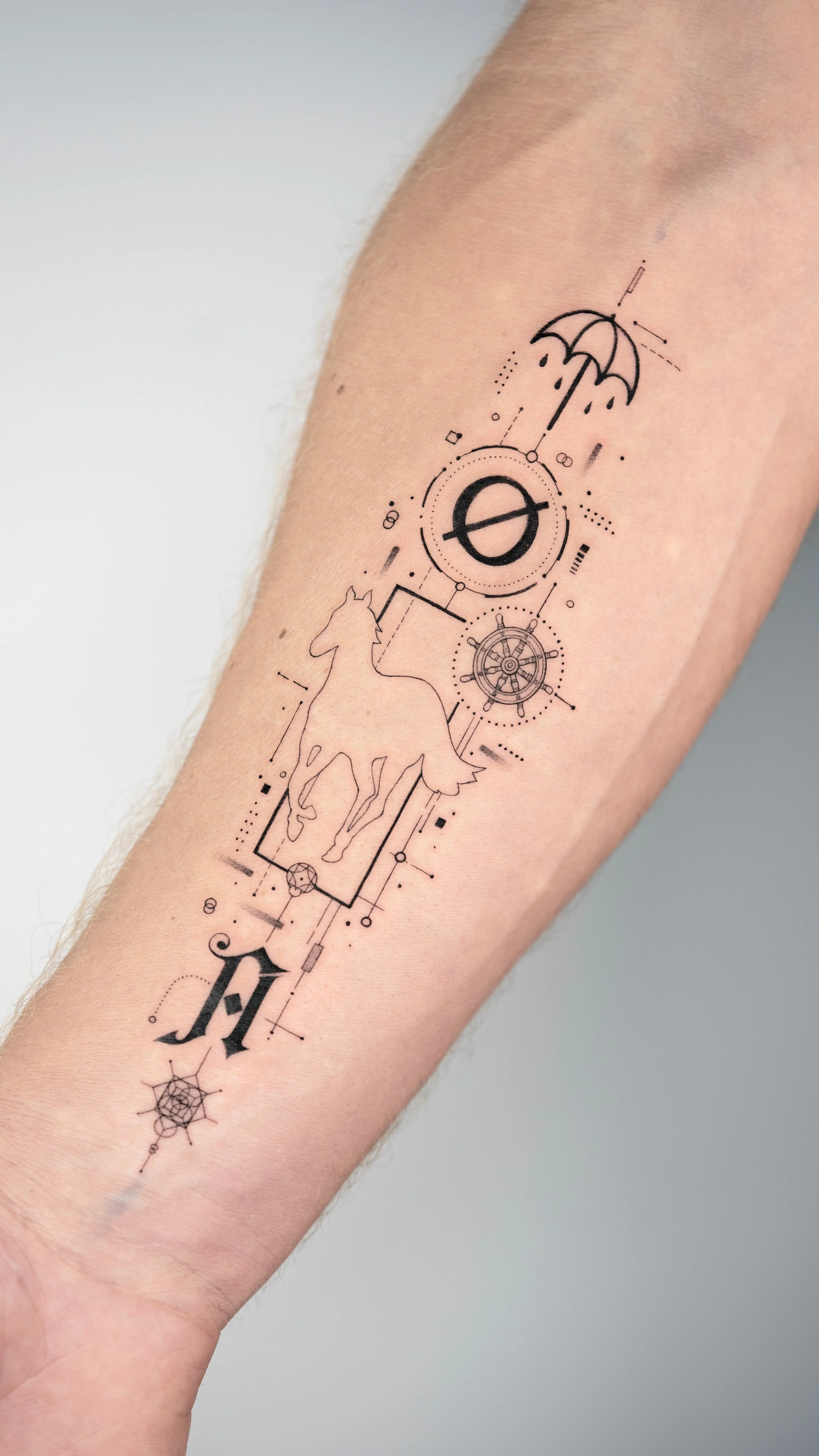 A tattoo on a person's forearm featuring a minimalist design with a horse inside a rectangle, a steering wheel, an umbrella with raindrops, a colon with a slash, a spider web, and various geometric elements and lines.