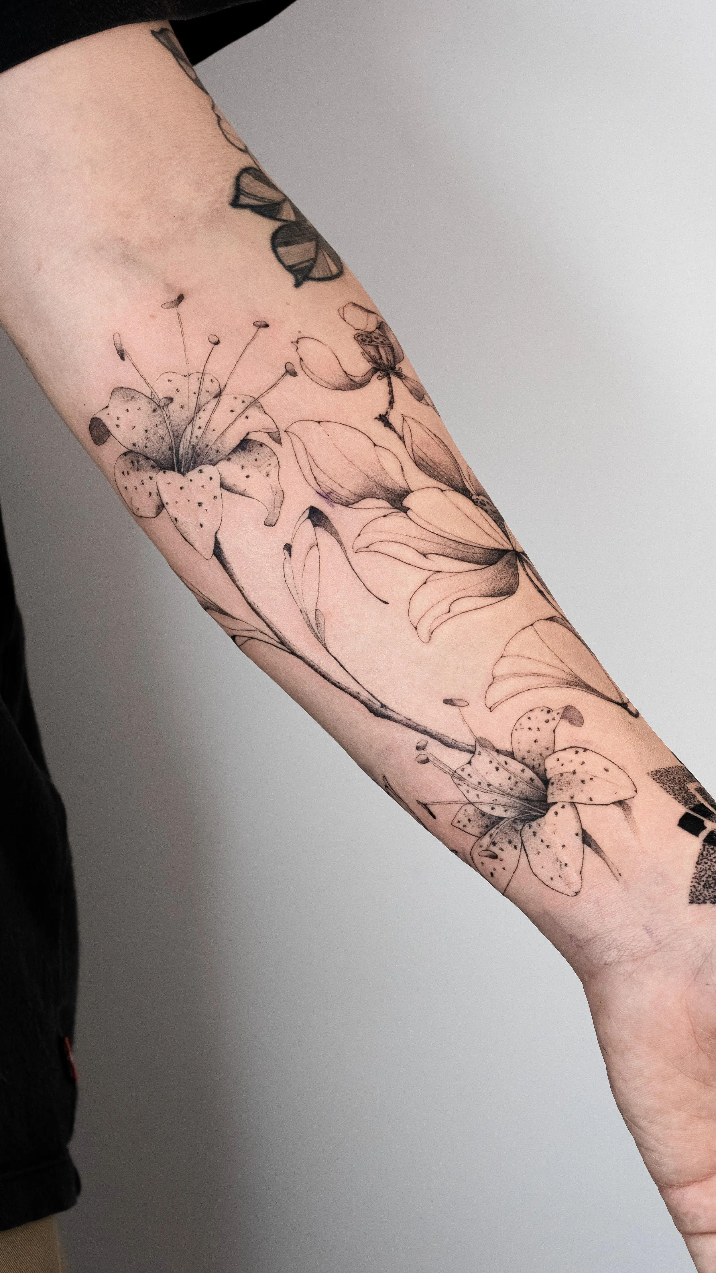 Black and gray floral tattoo on person's forearm featuring lilies and other flowers.