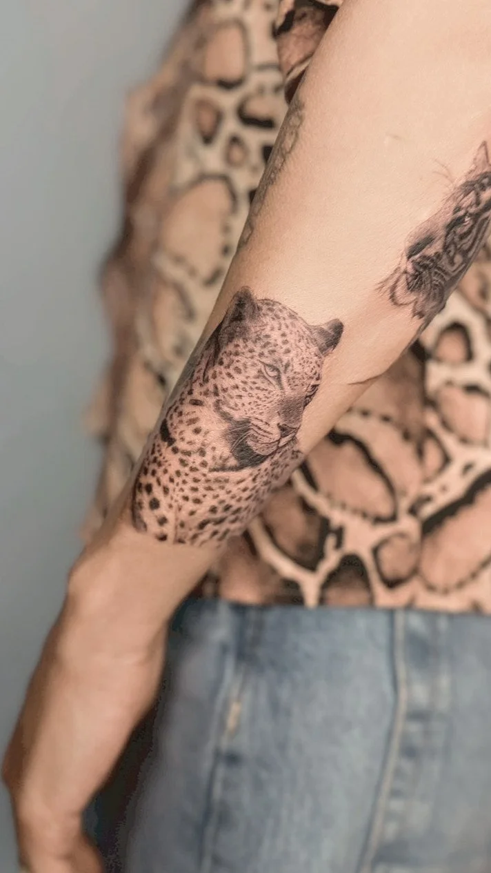 Tattoo of a cheetah's face on a person's forearm, with part of another tattoo visible nearby.