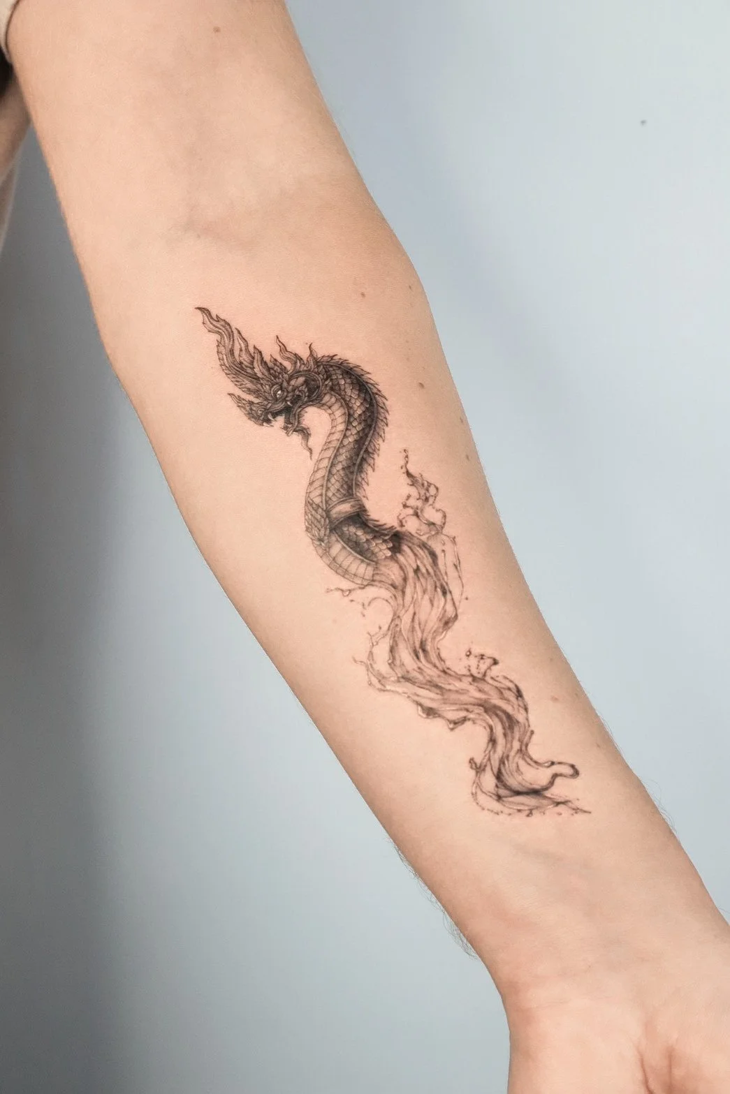 A black and gray tattoo of a dragon on a person's forearm.