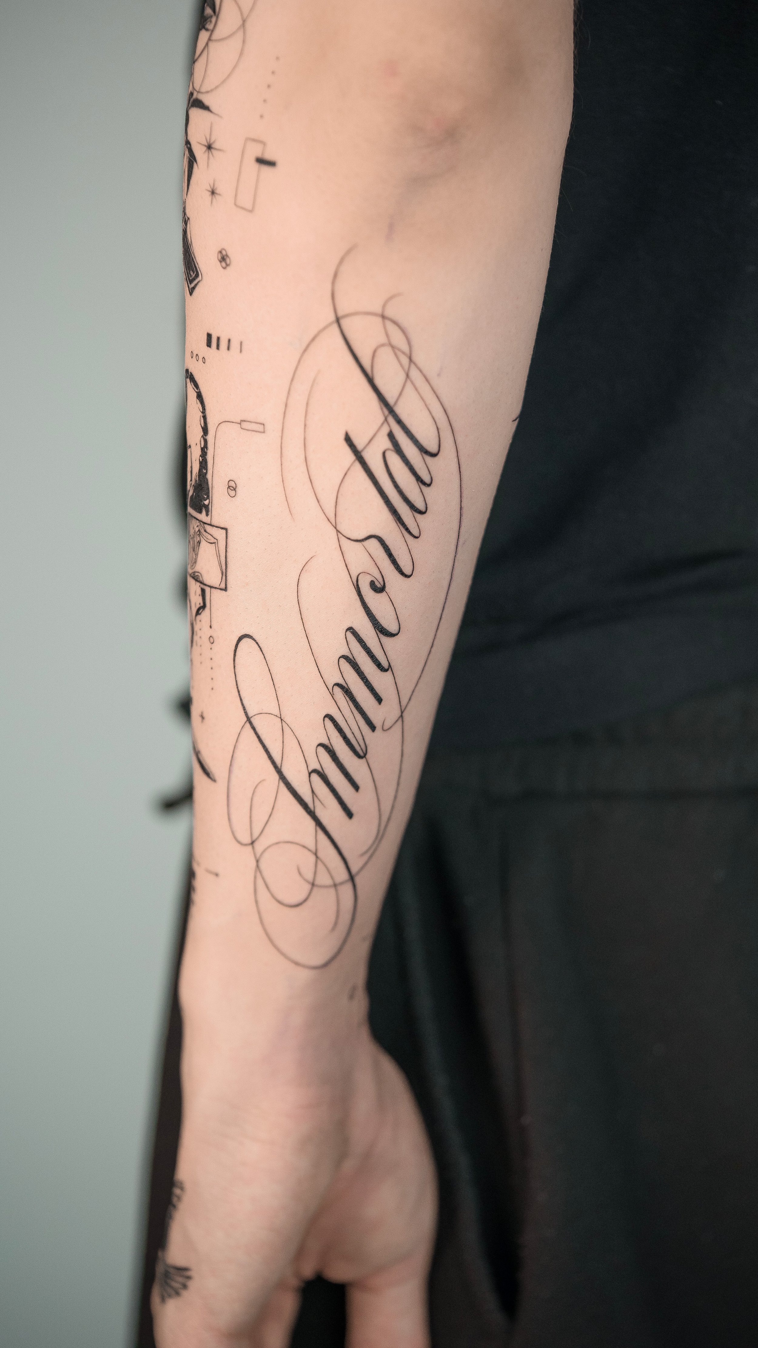A person's forearm with a tattoo of the word 'ambassador' in cursive script, along with small decorative sketches surrounding it.