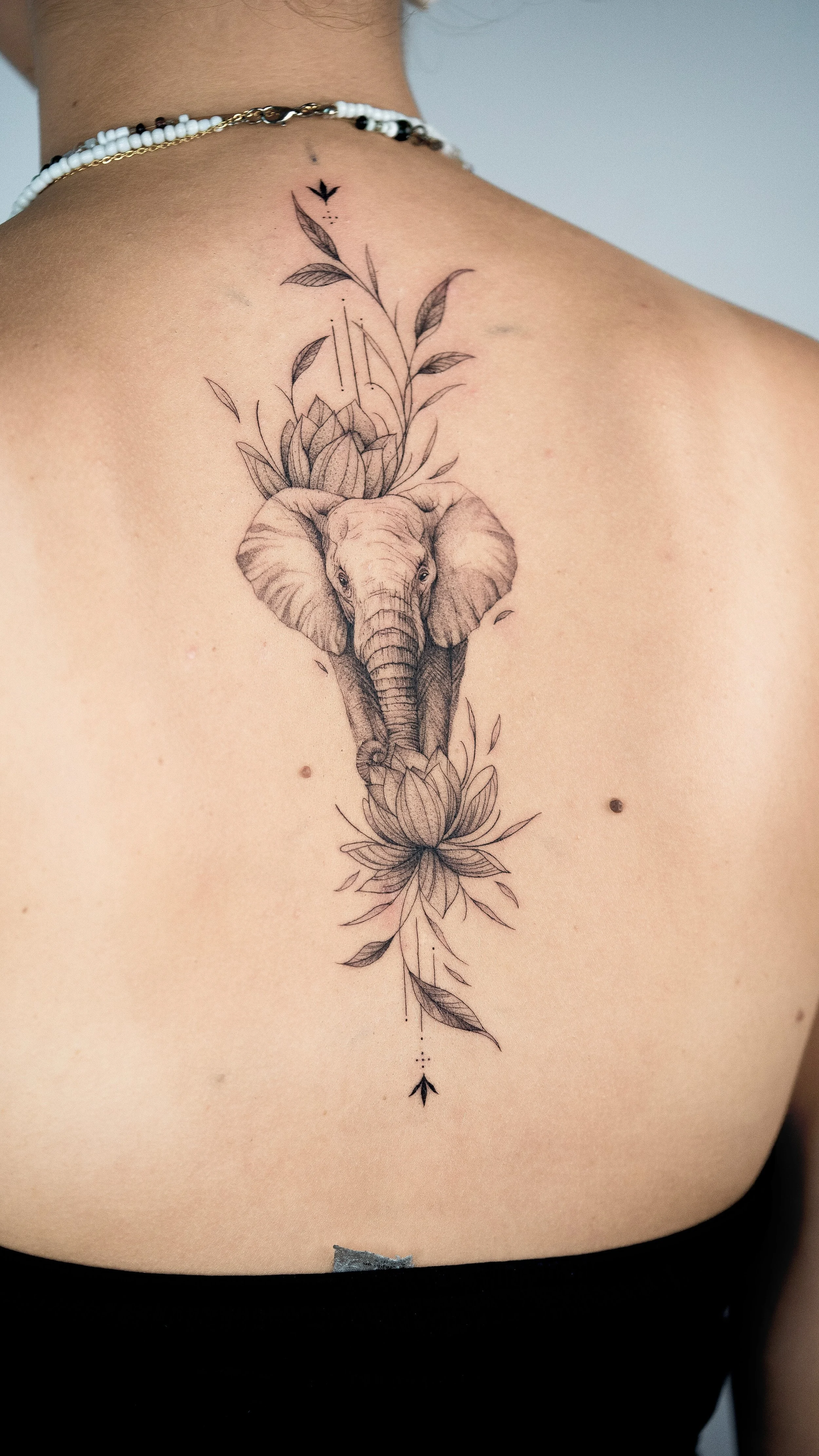 Tattoo of an elephant head with floral and leaf designs on a person's upper chest and shoulder.