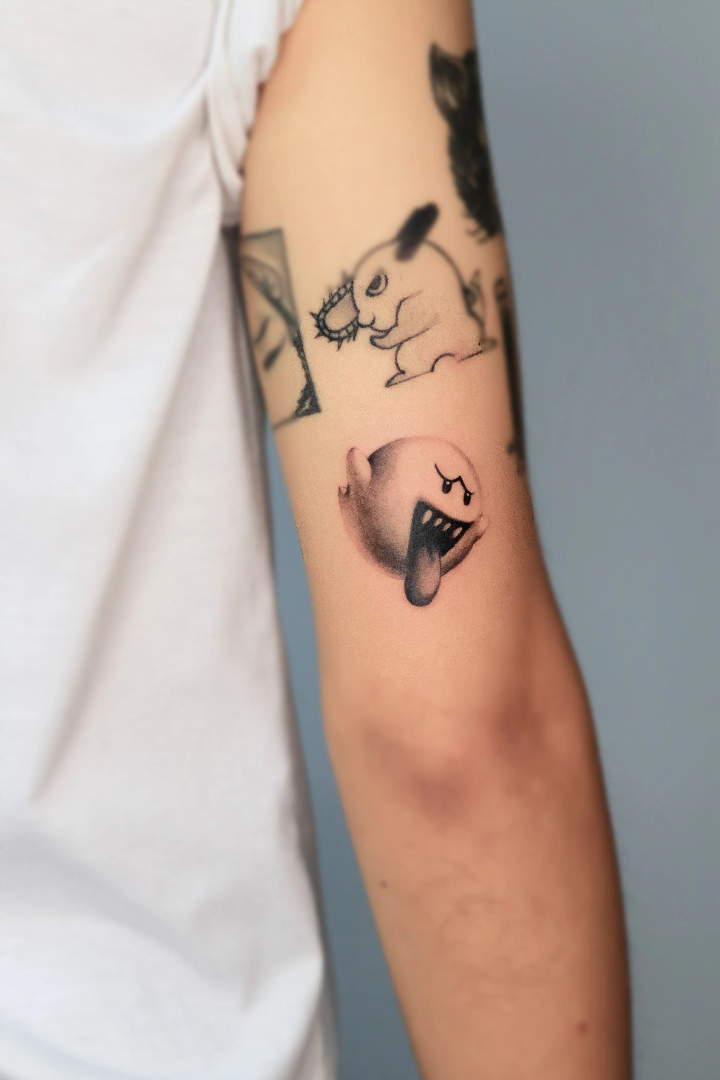 Tattoo of a cartoonish, screaming, grumpy ghost and a cute, smiling ghost on a person's upper arm.