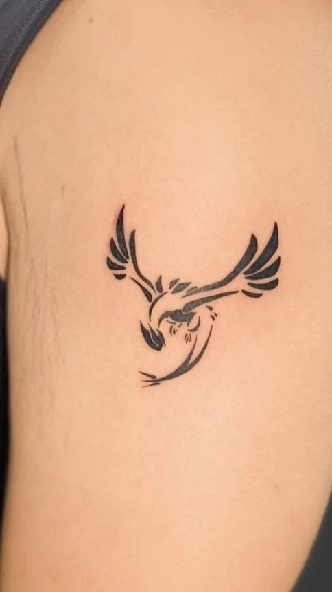 Black tribal-style tattoo of a bird with outstretched wings on upper arm.