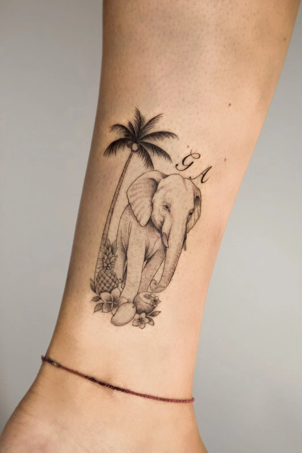 Tattoo of an elephant with tropical elements, including a palm tree, pineapple, coconuts, and flowers, with the initials 'GM' above.