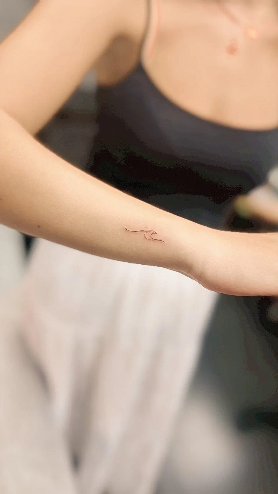 Close-up of a person's arm with a small, delicate tattoo of a wave on the forearm.