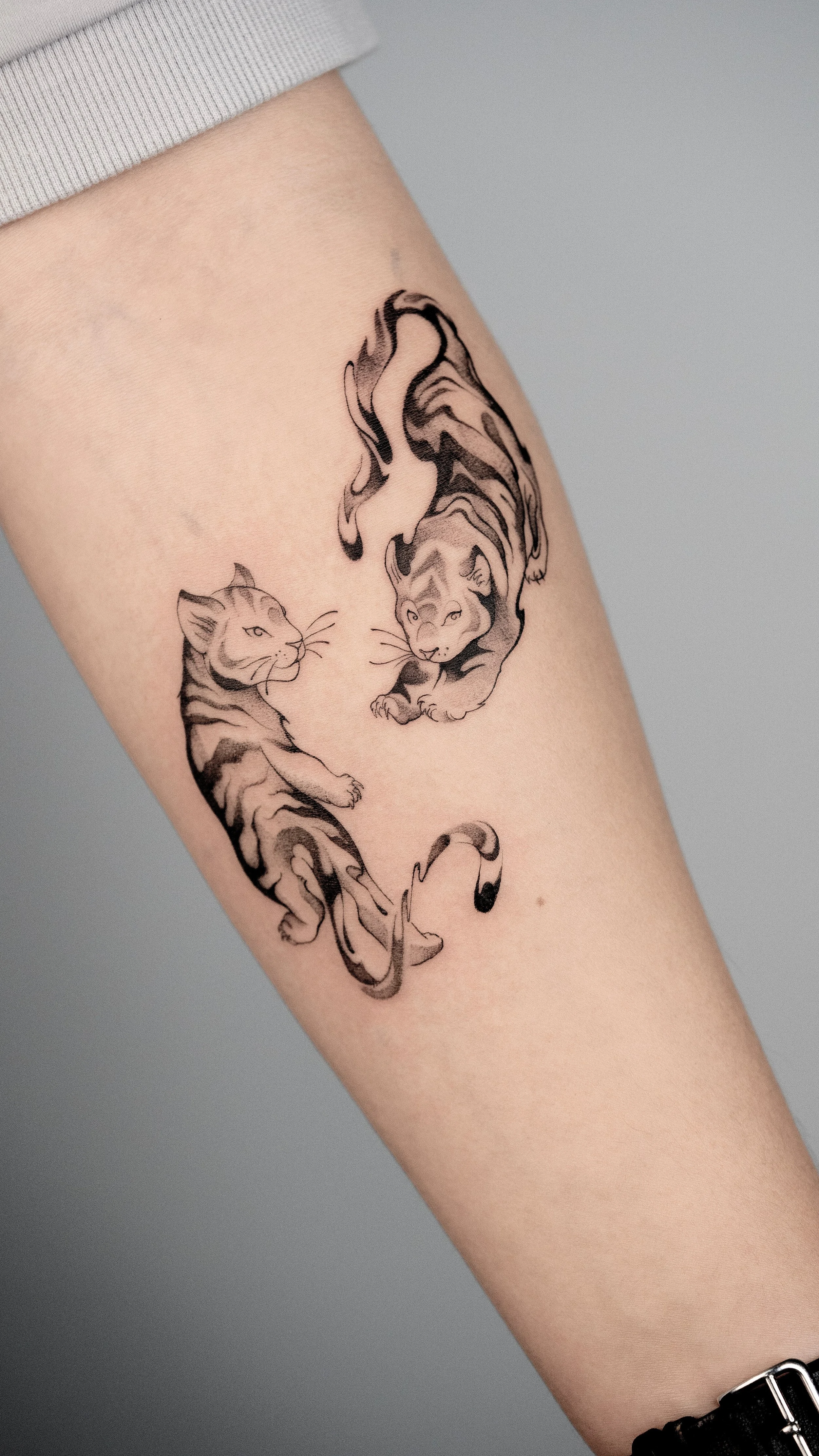 Tattoo of two tigers, one adult and one kitten, on person's arm.