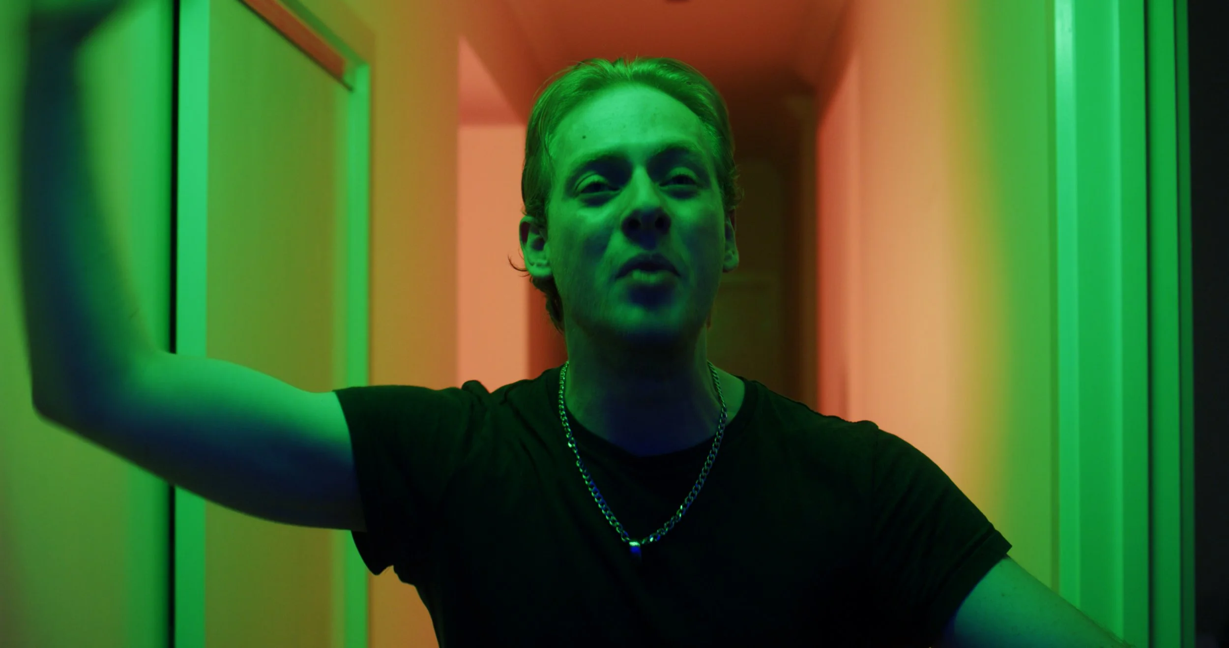 Person with arms raised in a hall with green and orange lighting.