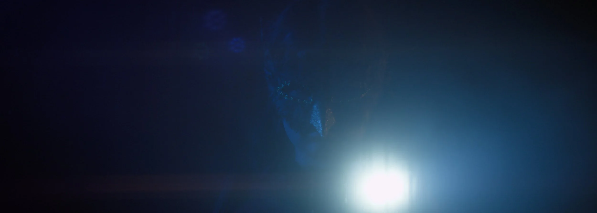 A dark, mysterious figure wearing a mask lit by a blue light, creating an eerie atmosphere.
Indoor dark lighting