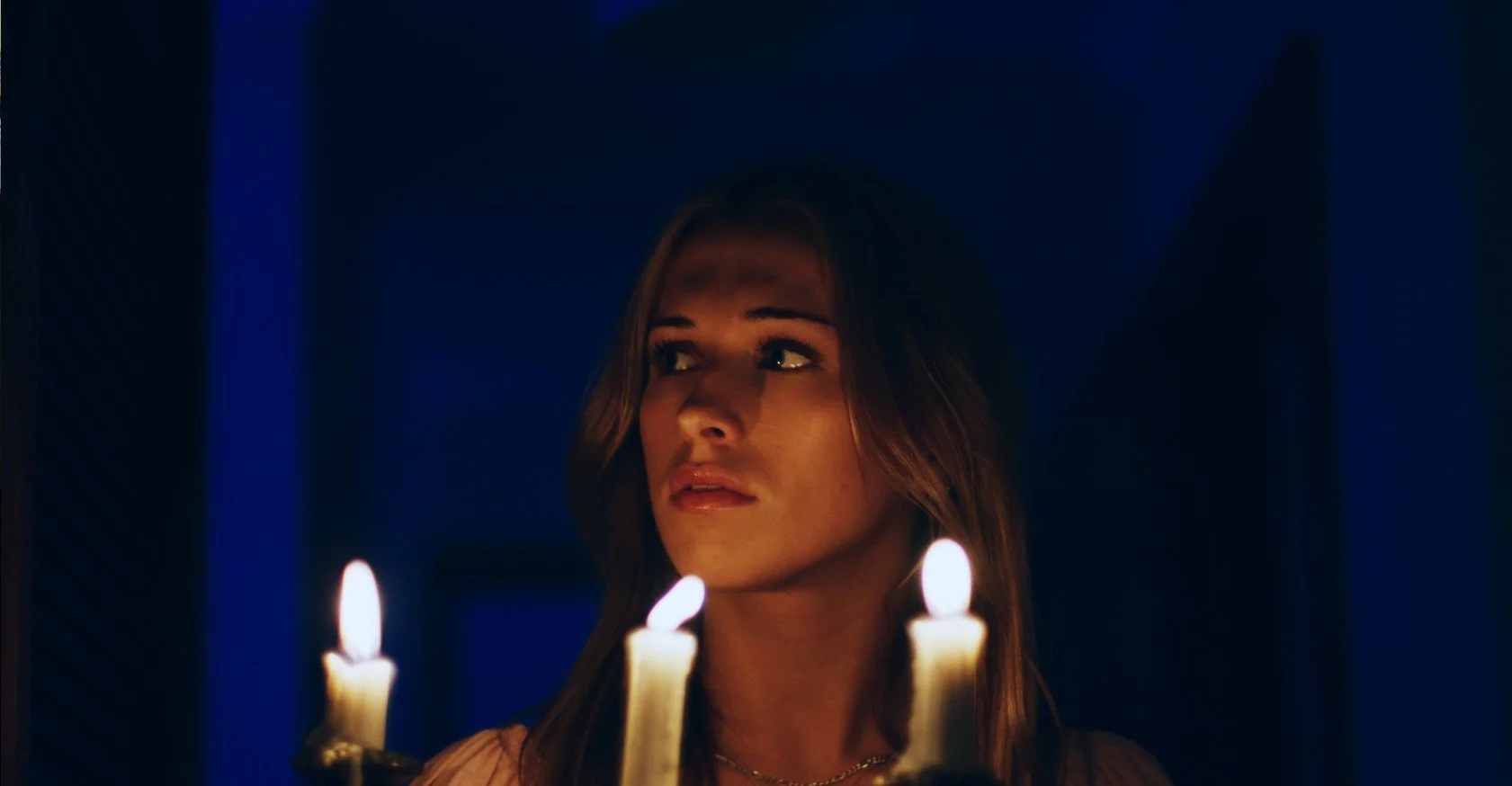 Woman looking to the side in dim light with candles in the foreground.
Indoor candle lit lighting.