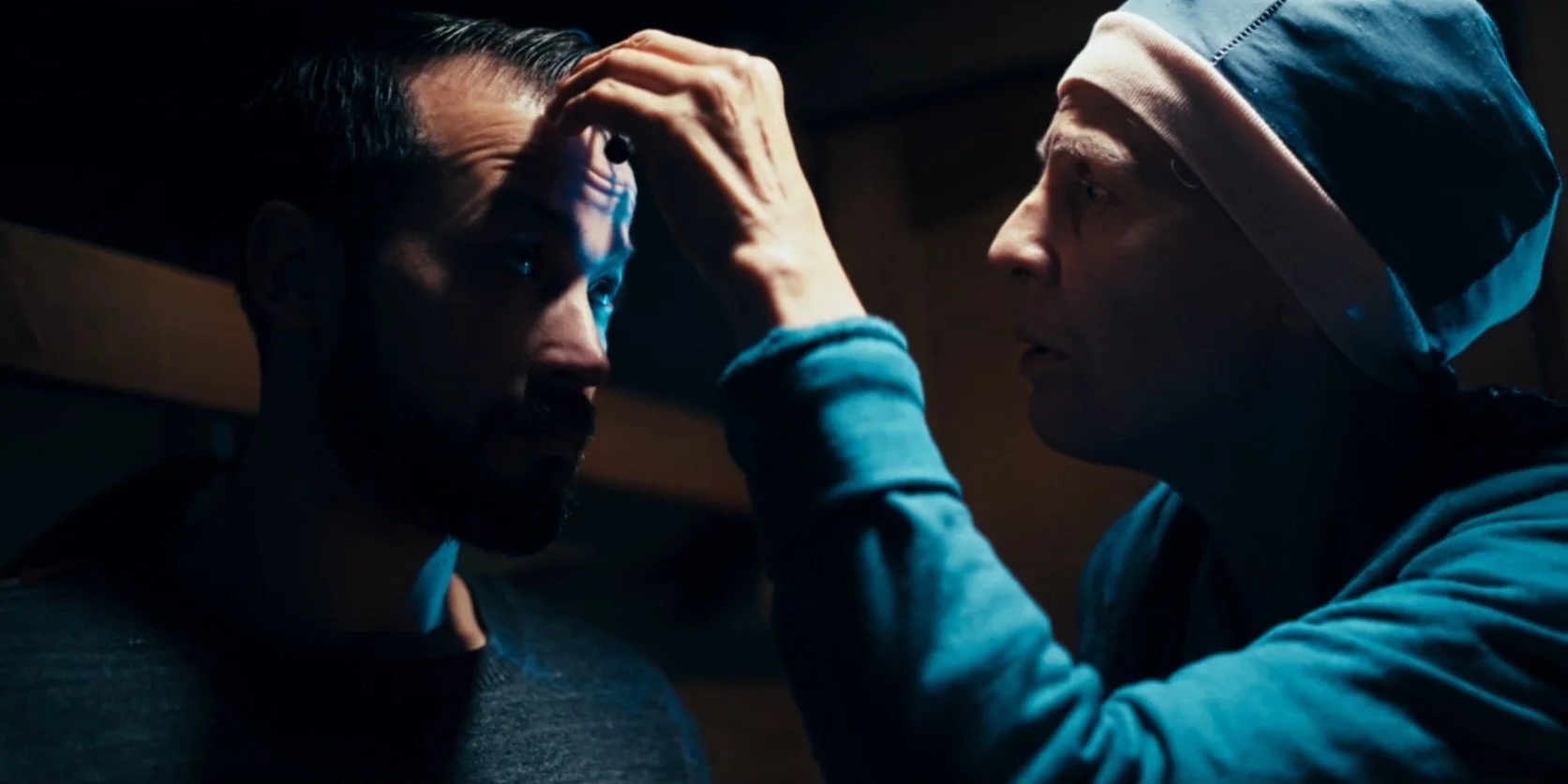 A person examining another person's forehead in a dimly lit room.