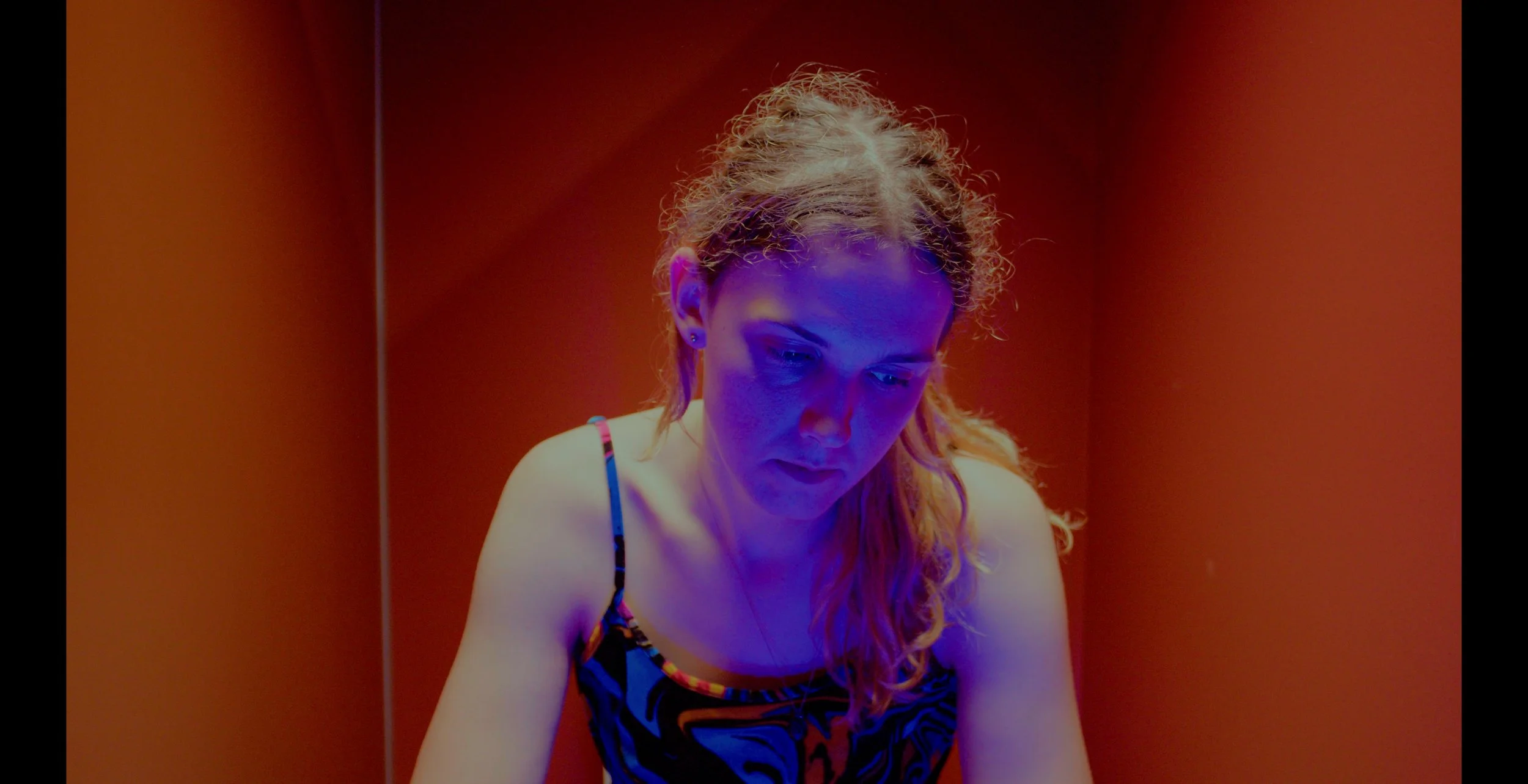 Person in a colorful dress bathed in blue light against a red background.