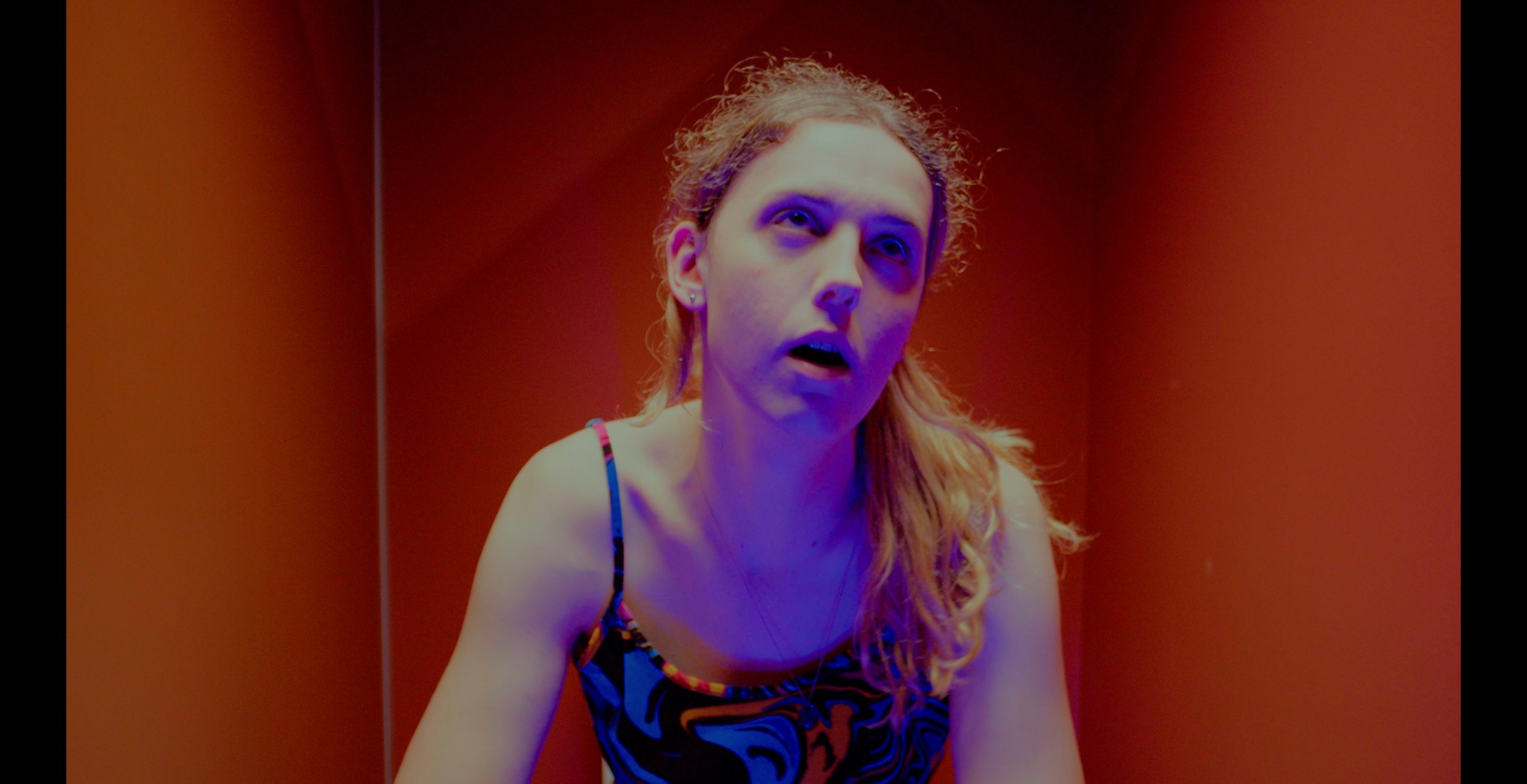 Person in colorful tank top under dramatic lighting with red background.