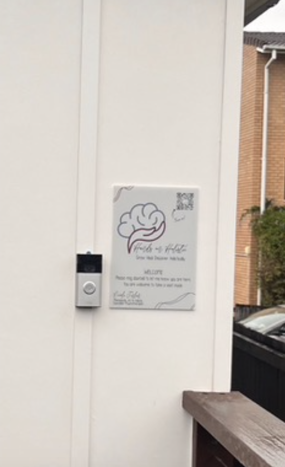 Hands On Holistic welcome sign against a white wall next to a silver doorbell