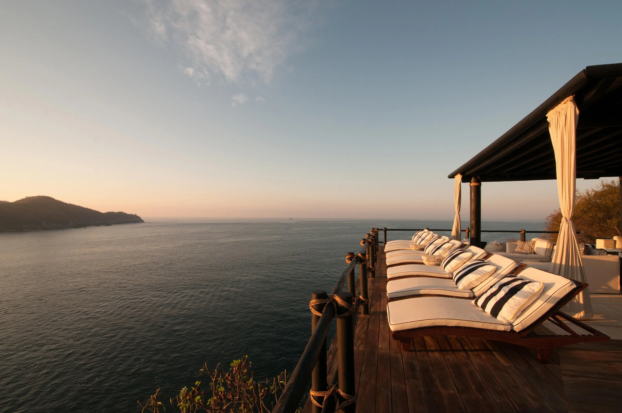 Ocean view at sunset with a wooden deck featuring lounge chairs and a canopy.