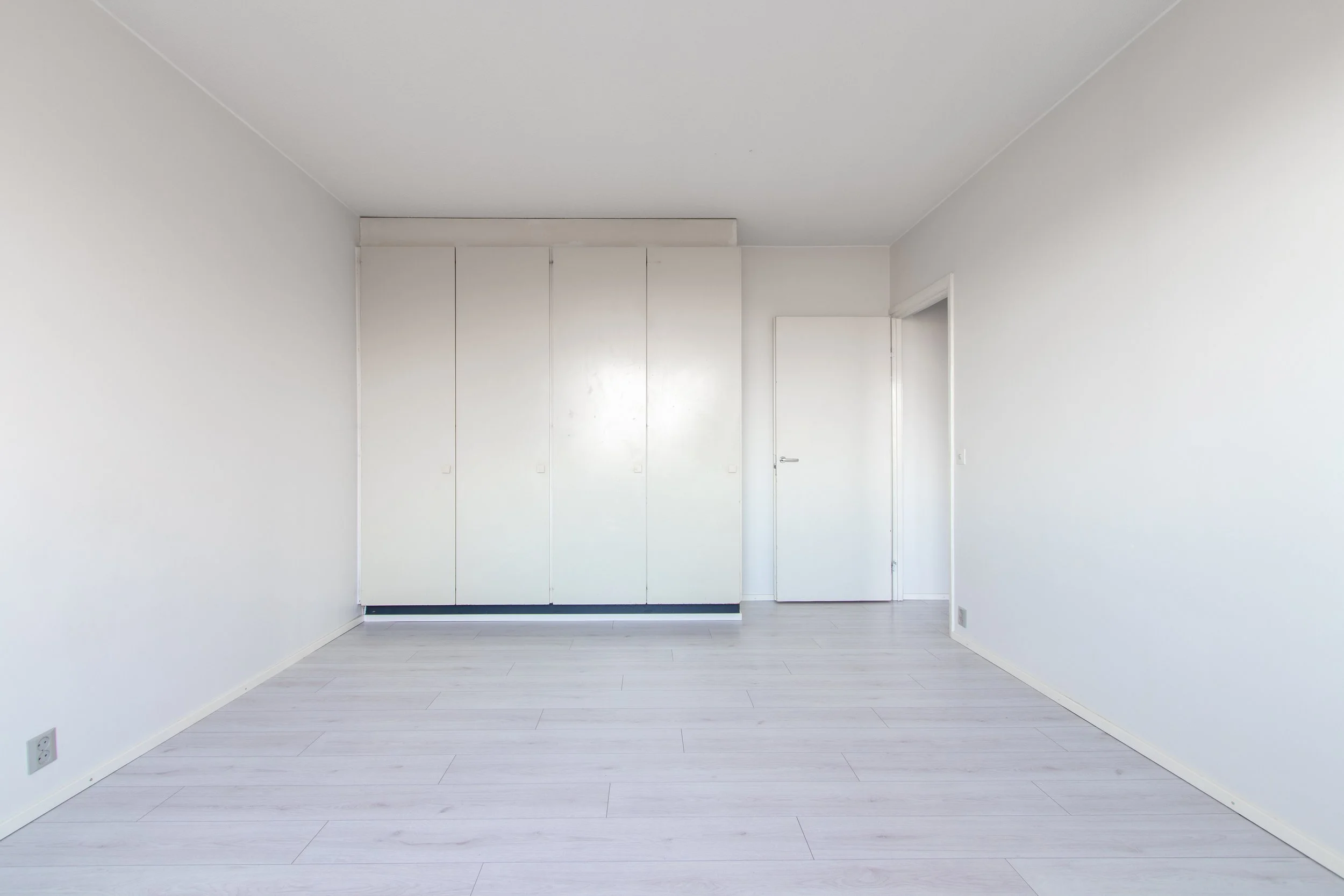 Tyhjä huone, vaaleat seinät ja lattia, vaatekaappi ja ovi.