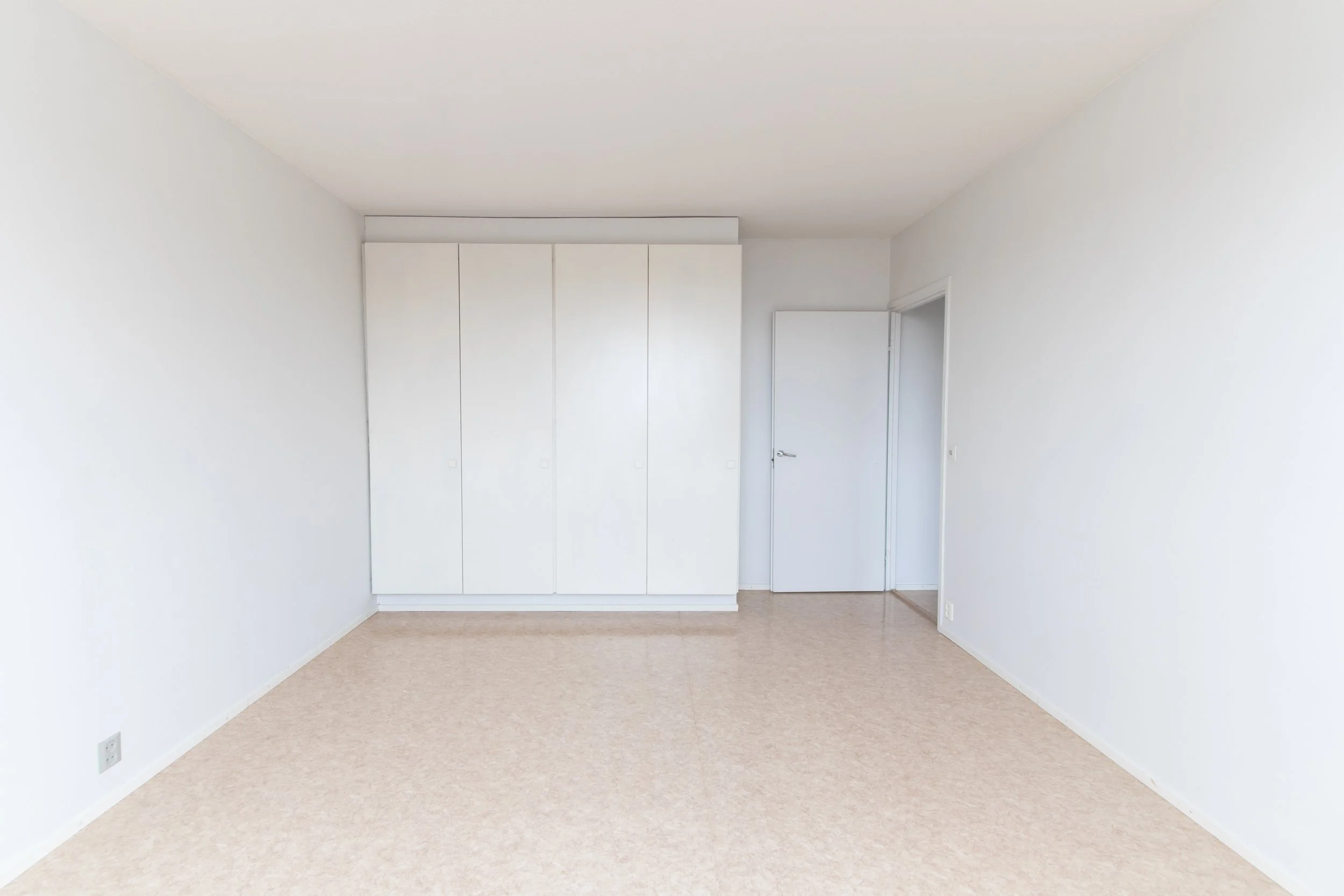 Tyhjä huone, valkoiset seinät, lipasto ja ovi.