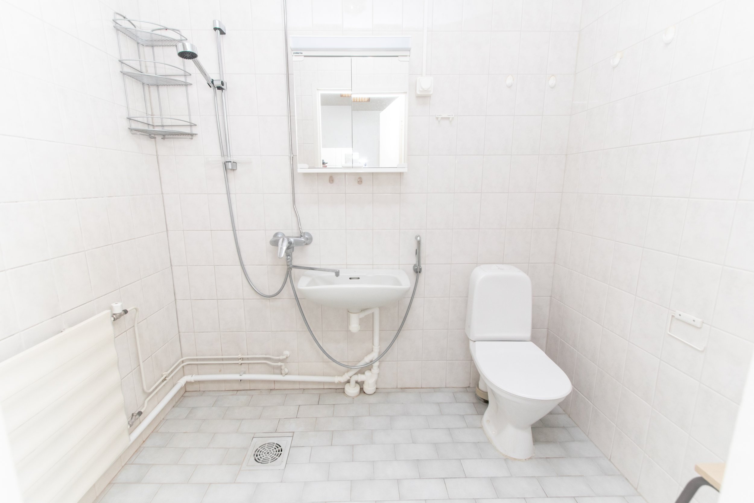 Pieni kylpyhuoneen tilavaallas, wc ja kylpyhuonevarusteet, valkoinen seinä ja lattia.